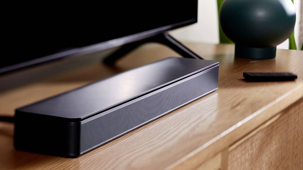 Una soundbar nera è posizionata su un mobile in legno accanto a un televisore e a un telecomando.