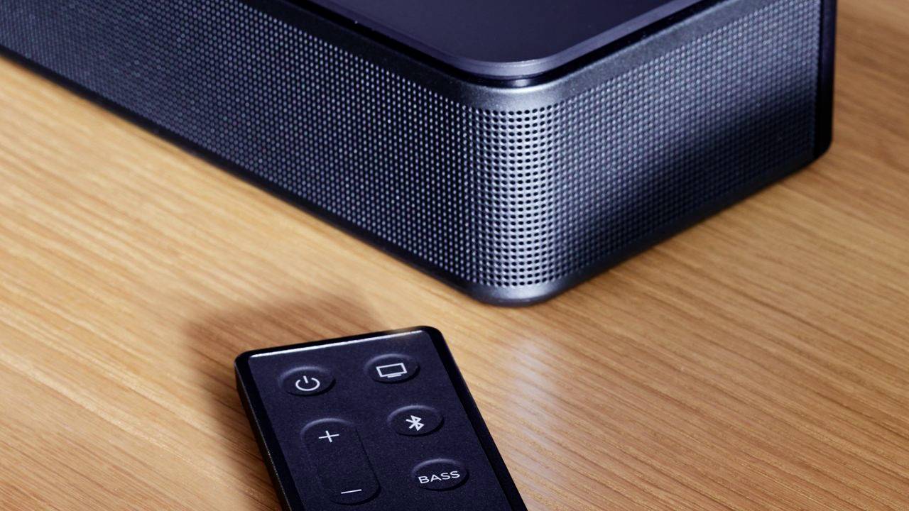 Un altoparlante nero e un telecomando su un tavolo di legno. Il telecomando ha tasti per il volume, il Bluetooth e il bass.