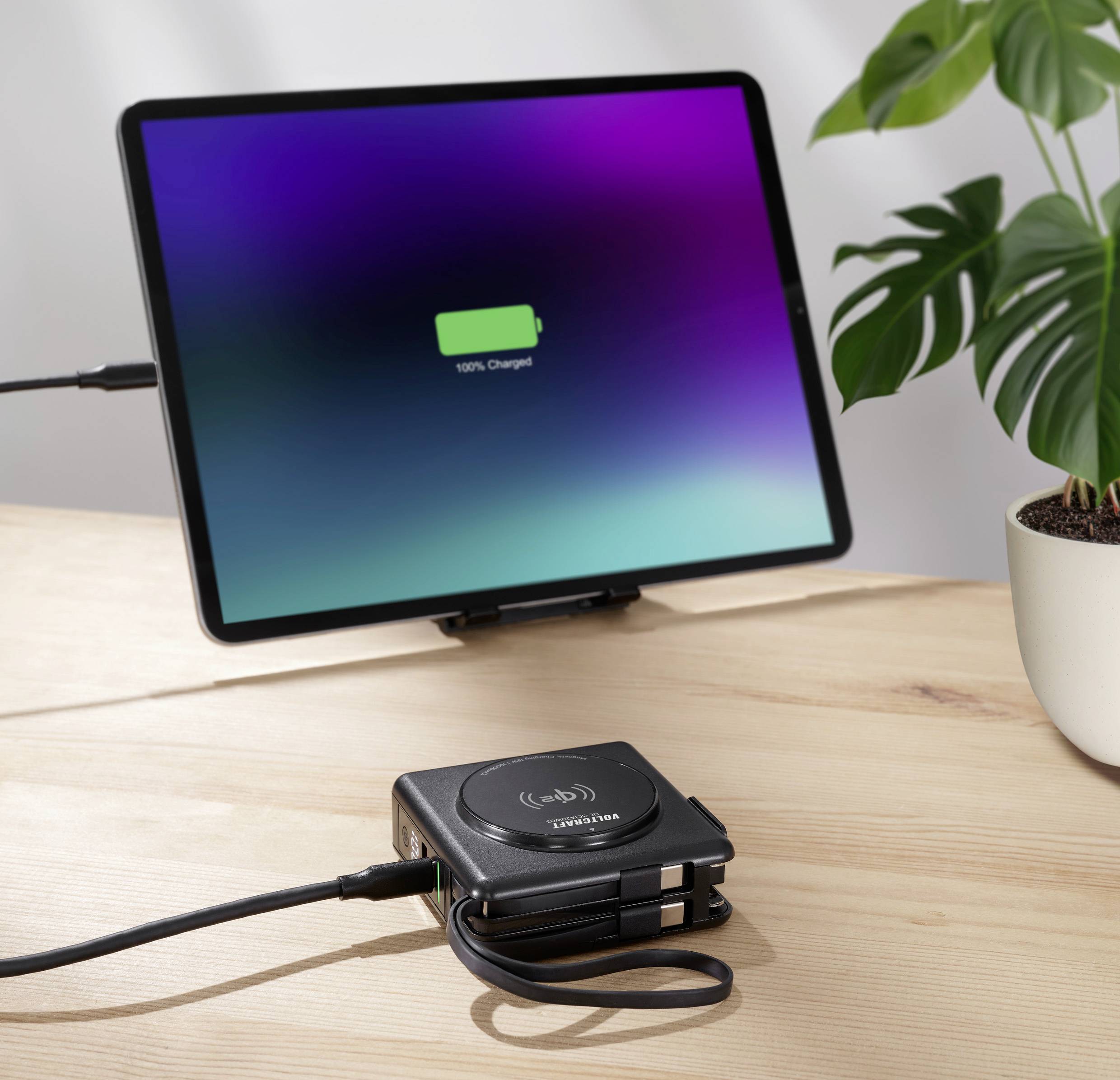 Un tablet con un simbolo di batteria completamente carica è poggiato su un tavolo. Accanto a esso c'è un caricabatterie wireless.