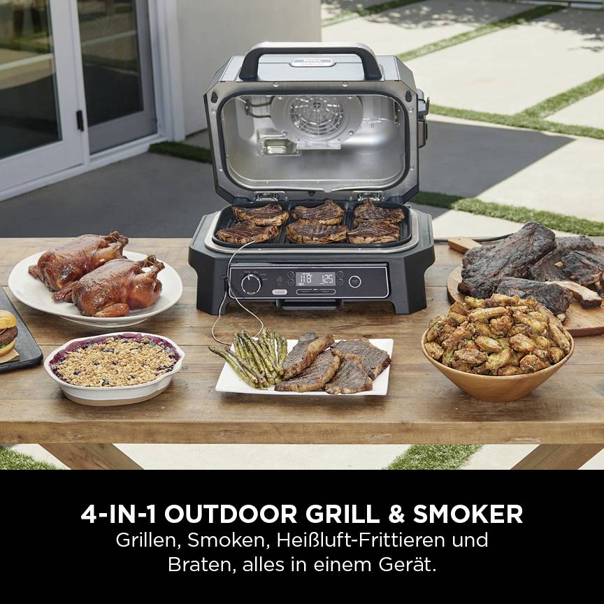 Un tavolo con un grill e affumicatore 4 in 1. Diversi cibi grigliati come carne e verdure sono distribuiti sui piatti.