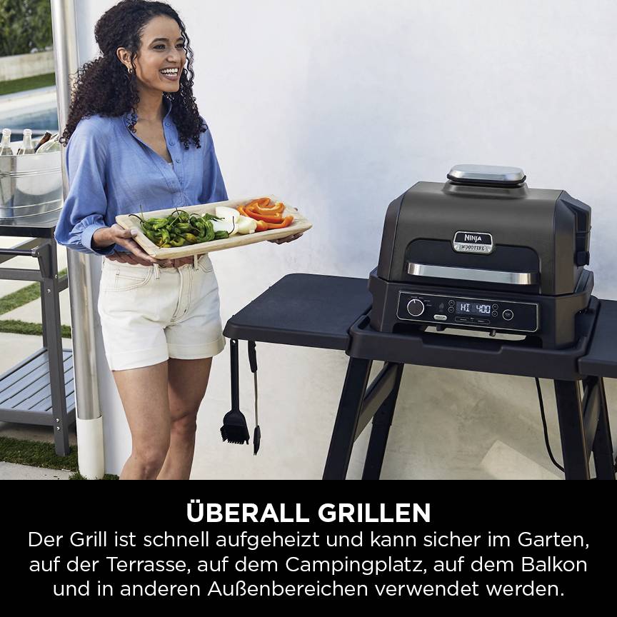 Una donna è in piedi accanto a un barbecue all'aperto con un vassoio pieno di verdure. Il barbecue mostra il logo "Überall Grillen".