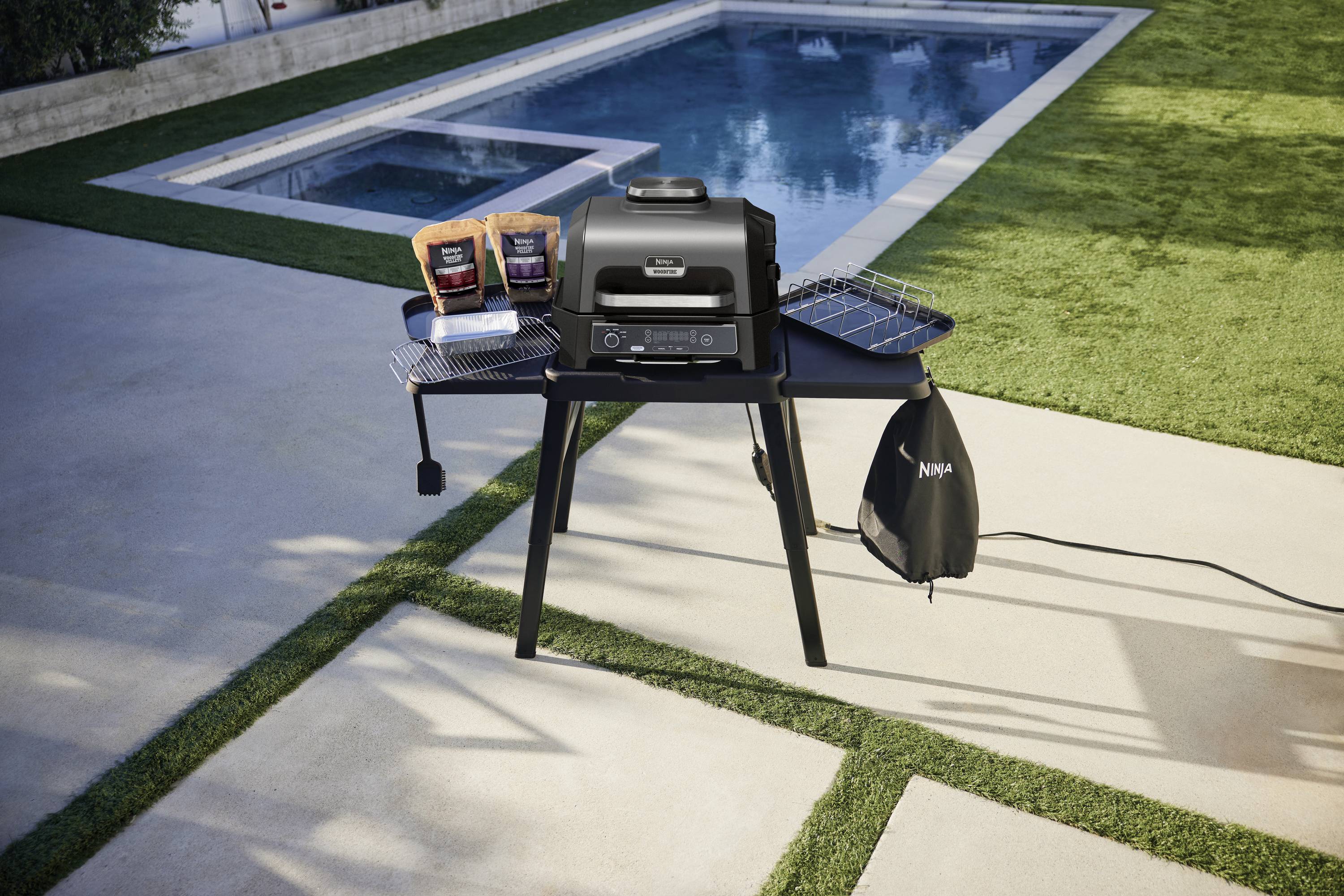 Barbecue a gas su una terrazza accanto a una piscina, con due sacchi di mattonelle di carbone sul tavolo.