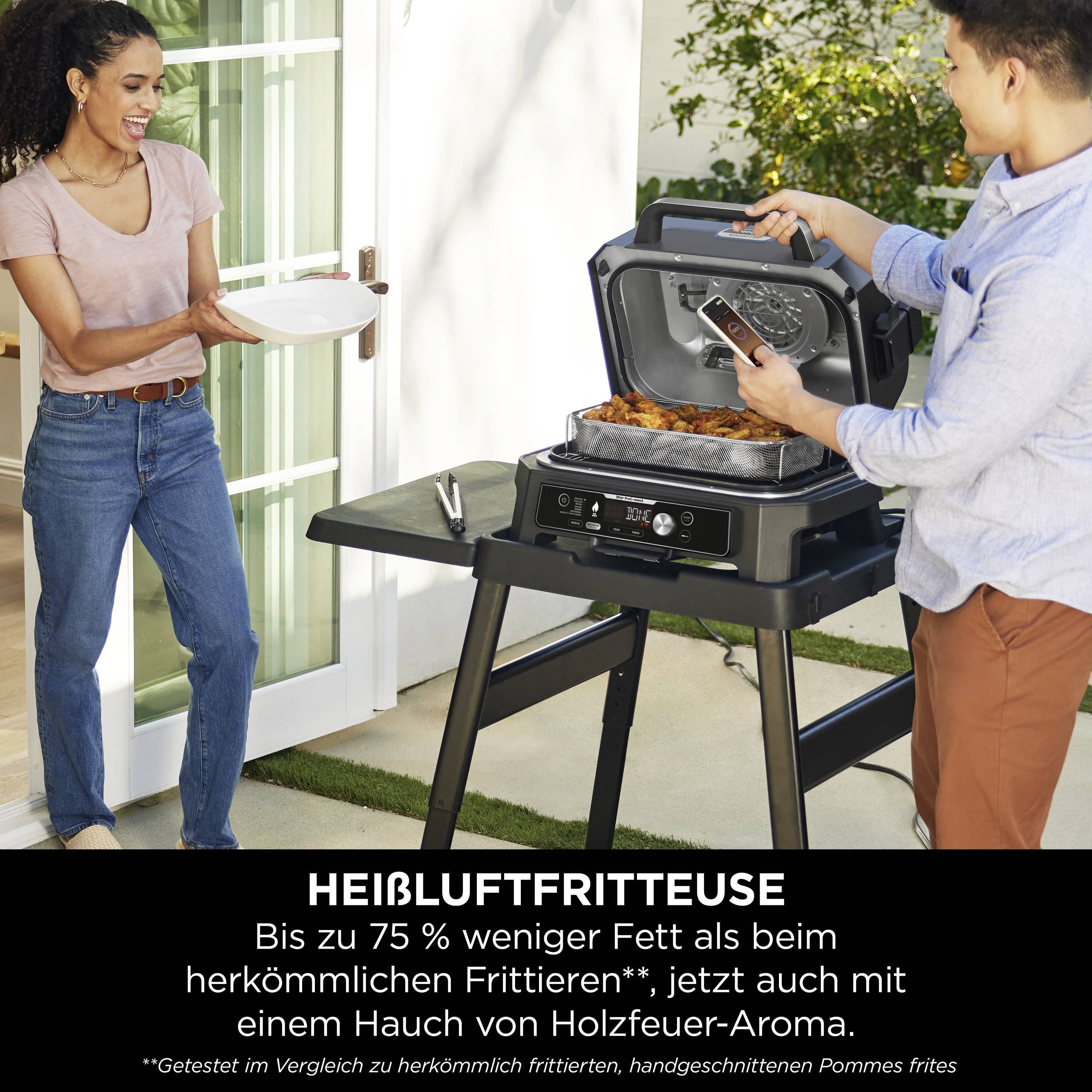 Una persona sta cucinando su un barbecue elettrico all'aperto e misura la temperatura, mentre un'altra persona tiene un piatto. Testo: 'Friggitrice ad aria calda con aroma di legna.'