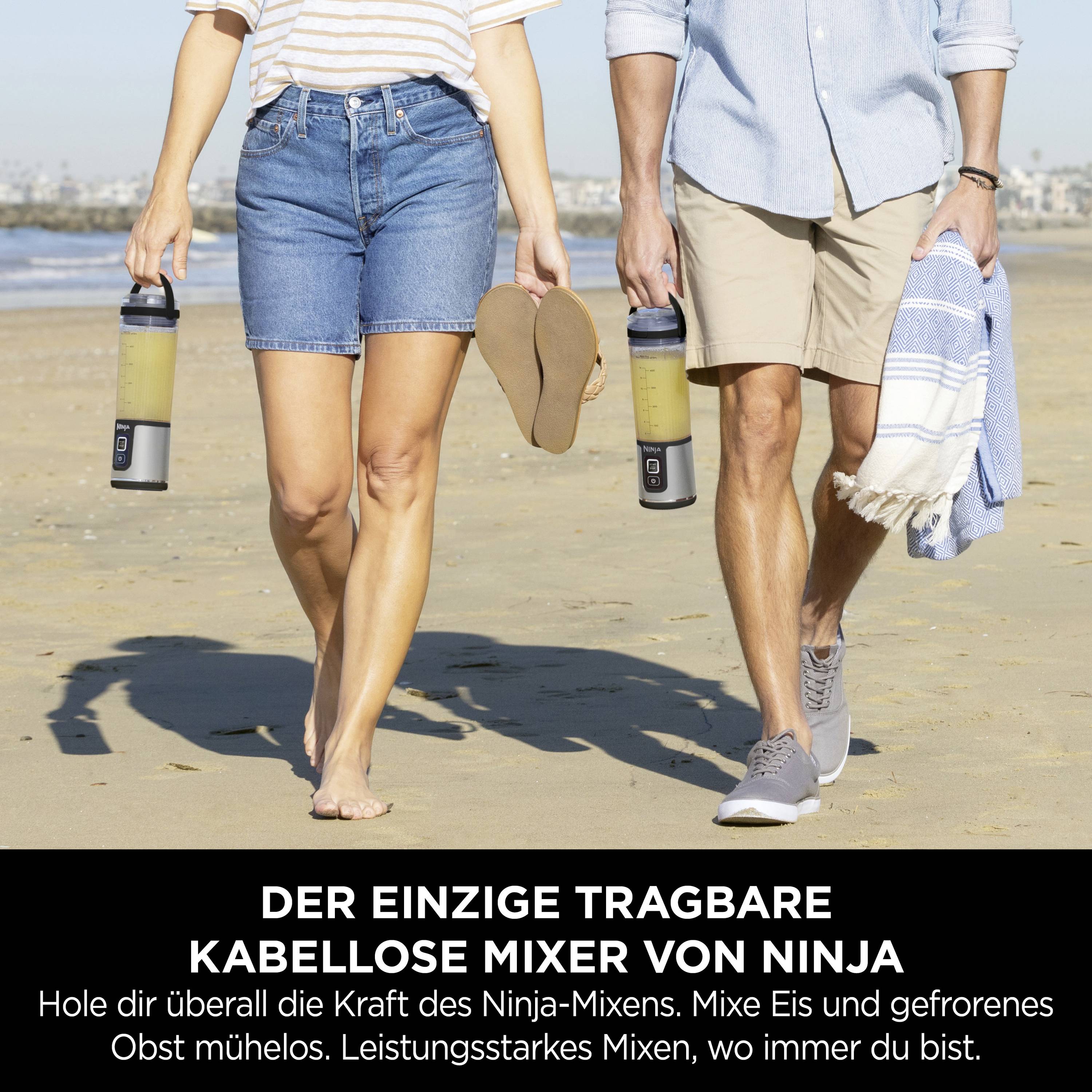 Due persone camminano sulla spiaggia, entrambe con mixer portatili ninja e bevande ghiacciate, con il sole e la città sullo sfondo.