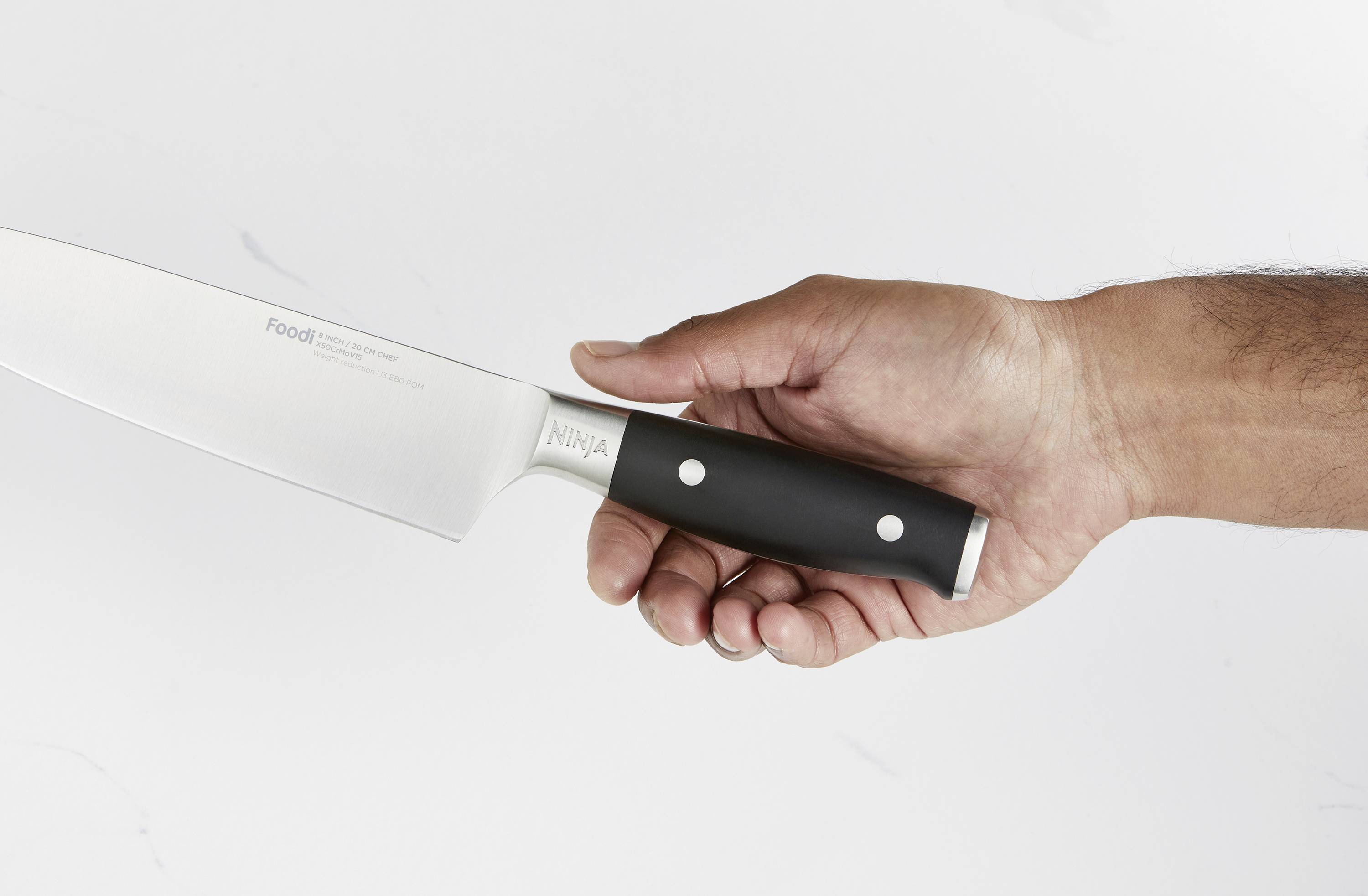 Una mano tiene un coltello da cucina con impugnatura nera e lama d'argento su uno sfondo bianco.