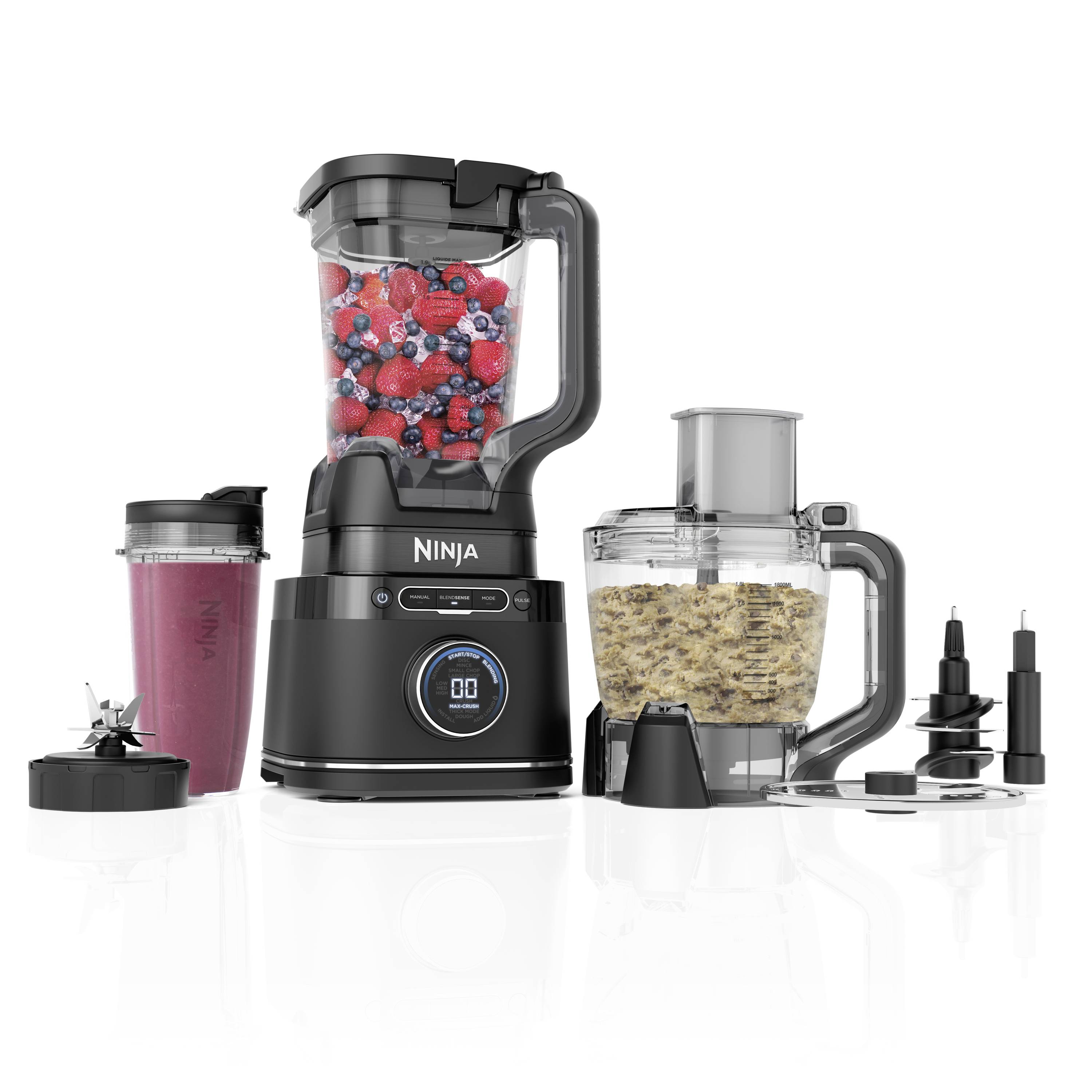 Un set di frullatore composto da frullatore, contenitore con bacche rosse, una ciotola con cereali macinati e tre diversi accessori per lame.