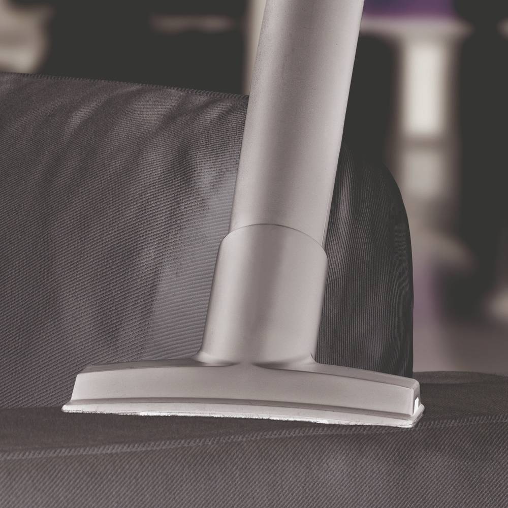 Un tubo dell'aspirapolvere aspira una fodera in tessuto grigio scuro. Sullo sfondo sono visibili colori sfocati.