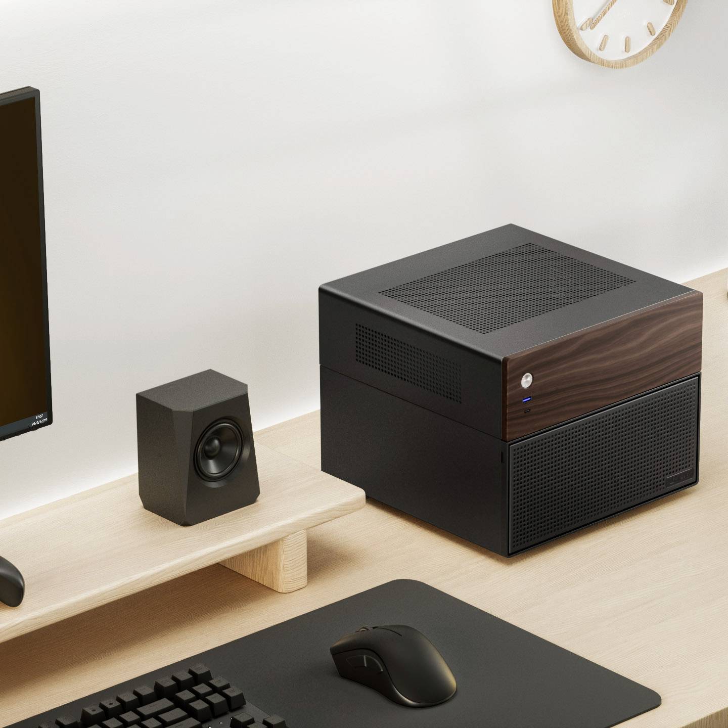 Un posto di lavoro moderno con computer, con un PC desktop compatto, monitor, altoparlanti, mouse e un orologio appeso alla parete.