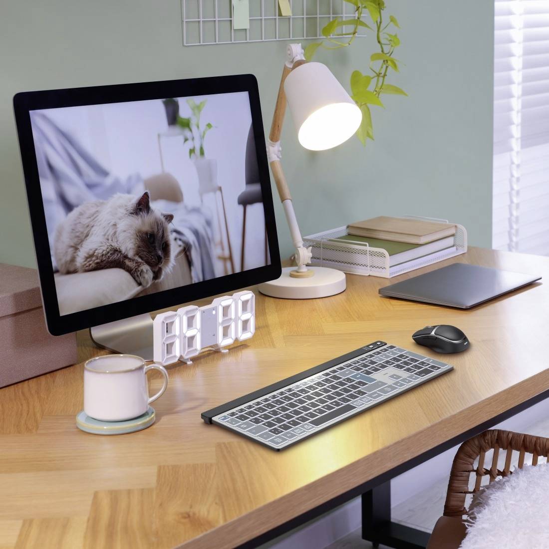 Una scrivania con un monitor del computer che mostra un gatto. Accanto ci sono una lampada, una tazza e una tastiera.