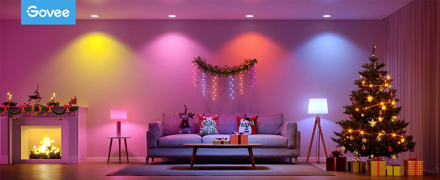 Soggiorno illuminato a colori con decorazioni natalizie, divano con cuscini, tavolo con regali, albero di Natale addobbato e fuoco nel camino.