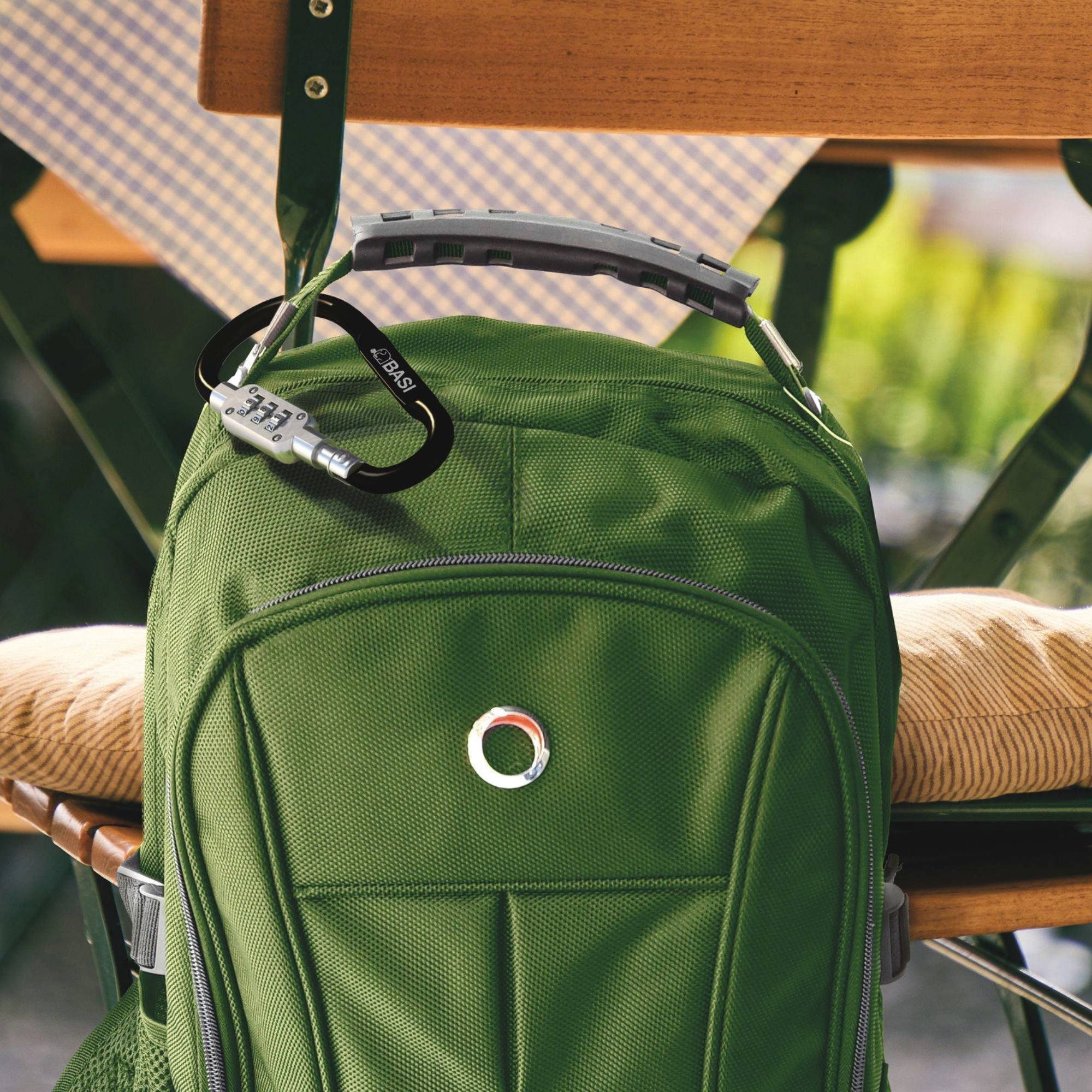 Uno zaino verde è appeso a una sedia con un piccolo lucchetto sui suoi zip; posizionato all'aperto.
