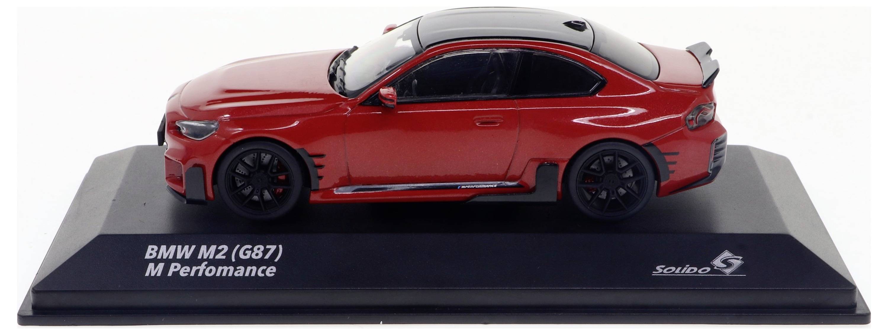Modellino di un'auto BMW M2 (G87) M Performance di colore rosso su un piedistallo nero. Vista laterale con cerchi neri e dettagli.