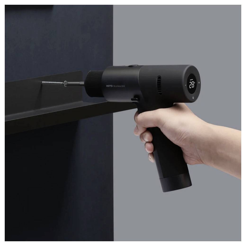 Una mano impugna un cacciavite elettrico nero, avvitandolo in un pezzo di legno scuro. Il display del cacciavite mostra '28'.