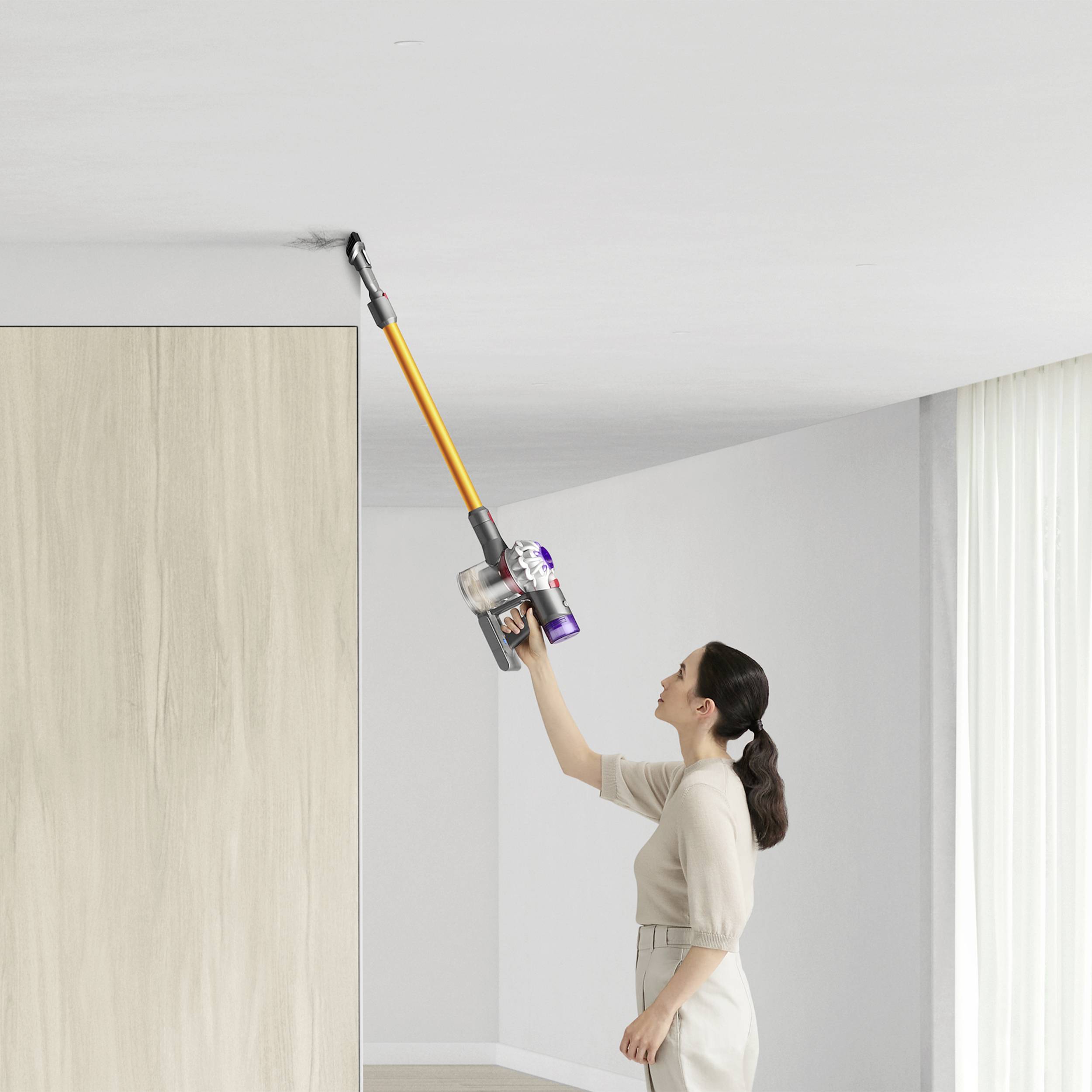 Una donna pulisce il soffitto con un aspirapolvere senza fili in una stanza luminosa e arredata in stile moderno.