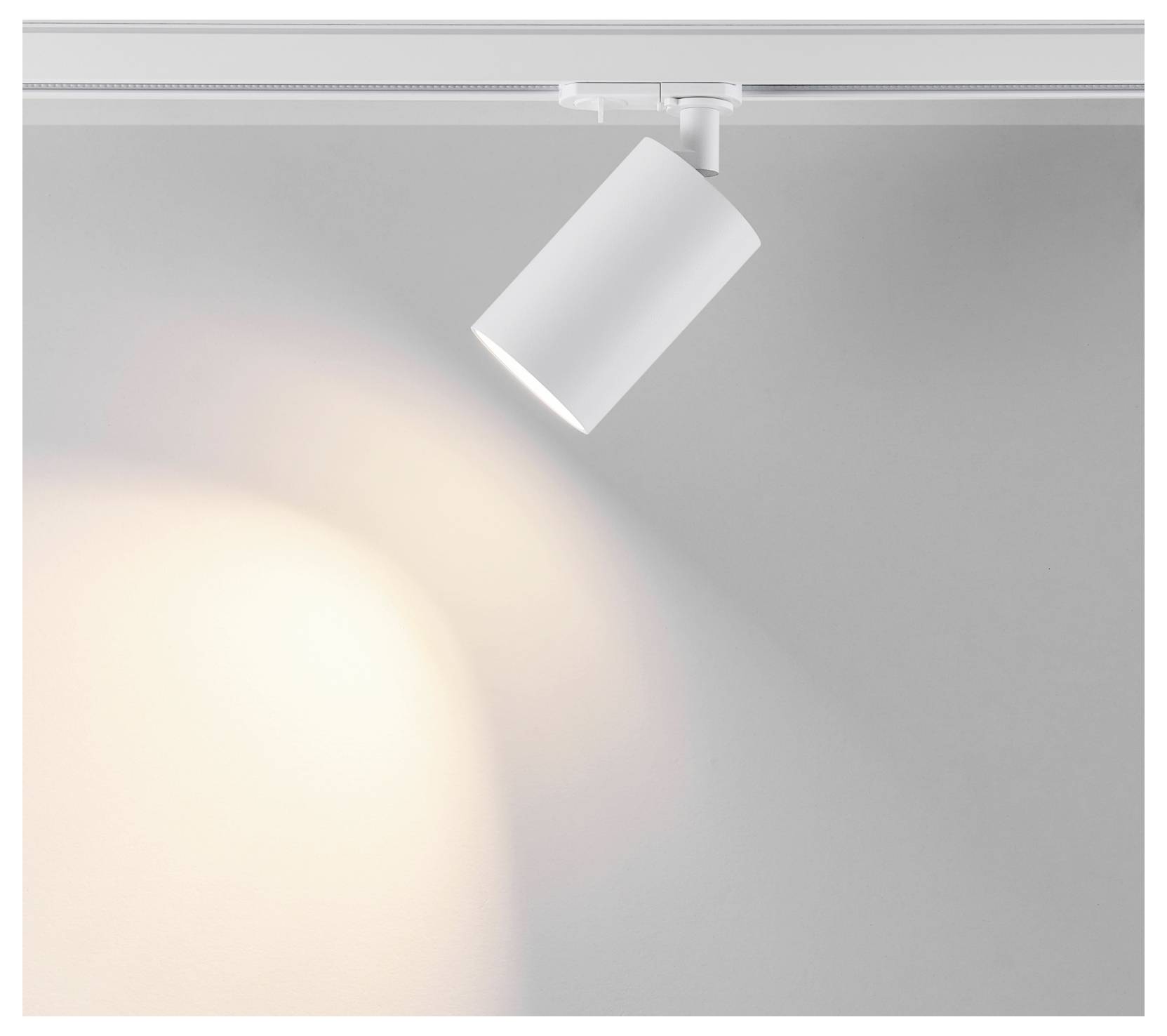 Faretto a binario bianco su una guida a soffitto che proietta un fascio di luce calda su una parete grigia.