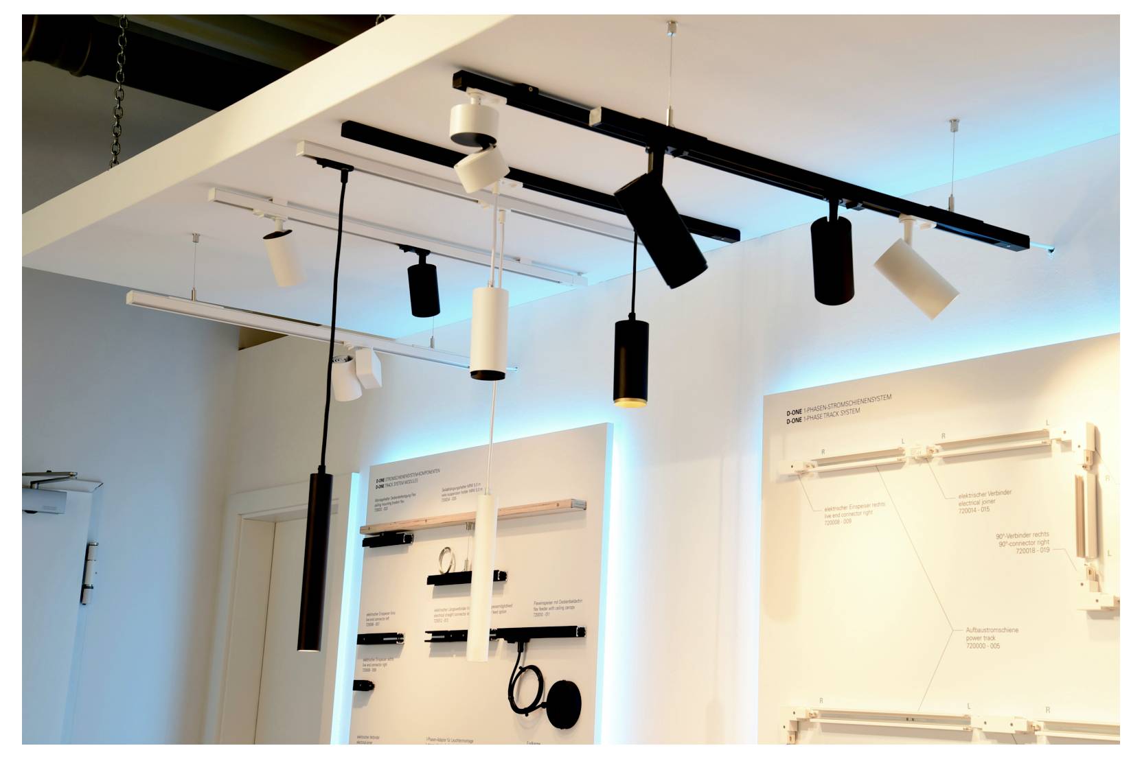 Illuminazione a binario da soffitto con più faretti sospesi regolabili sopra pannelli espositivi da parete illuminati.