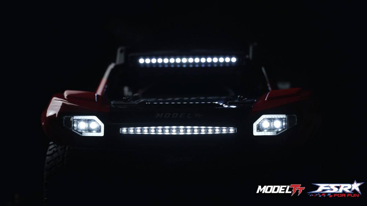 Un'auto telecomandata illuminata anteriormente, su uno sfondo scuro. Scritta 'MODEL' visibile sul lato anteriore. Loghi in basso a destra.