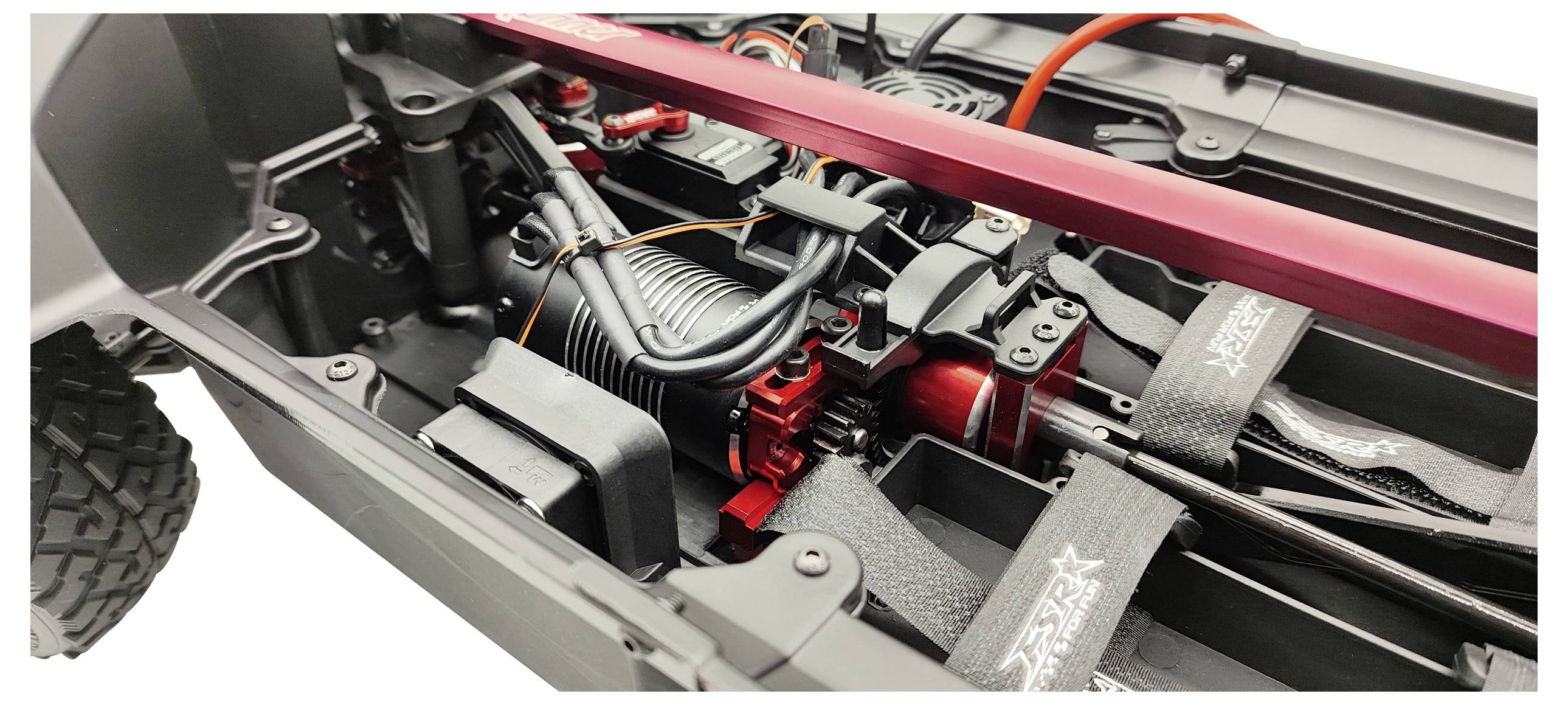 Primo piano di un'auto radiocomandata con focus sul motore, cablaggio e componenti di sospensione nel telaio. Design dinamico chiaramente visibile.
