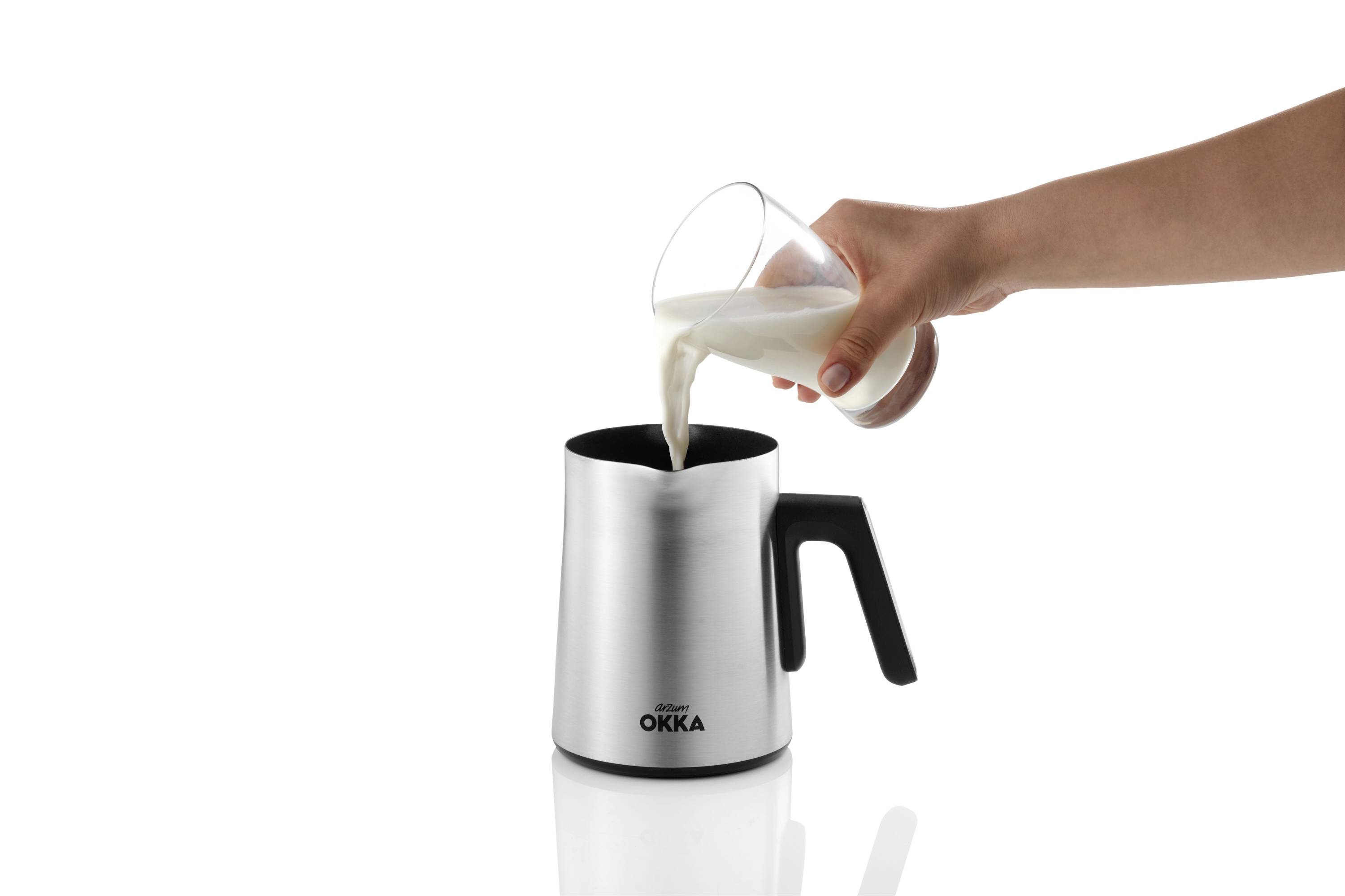 Una mano versa il latte da un bicchiere in una brocca da latte d'argento con manico nero.