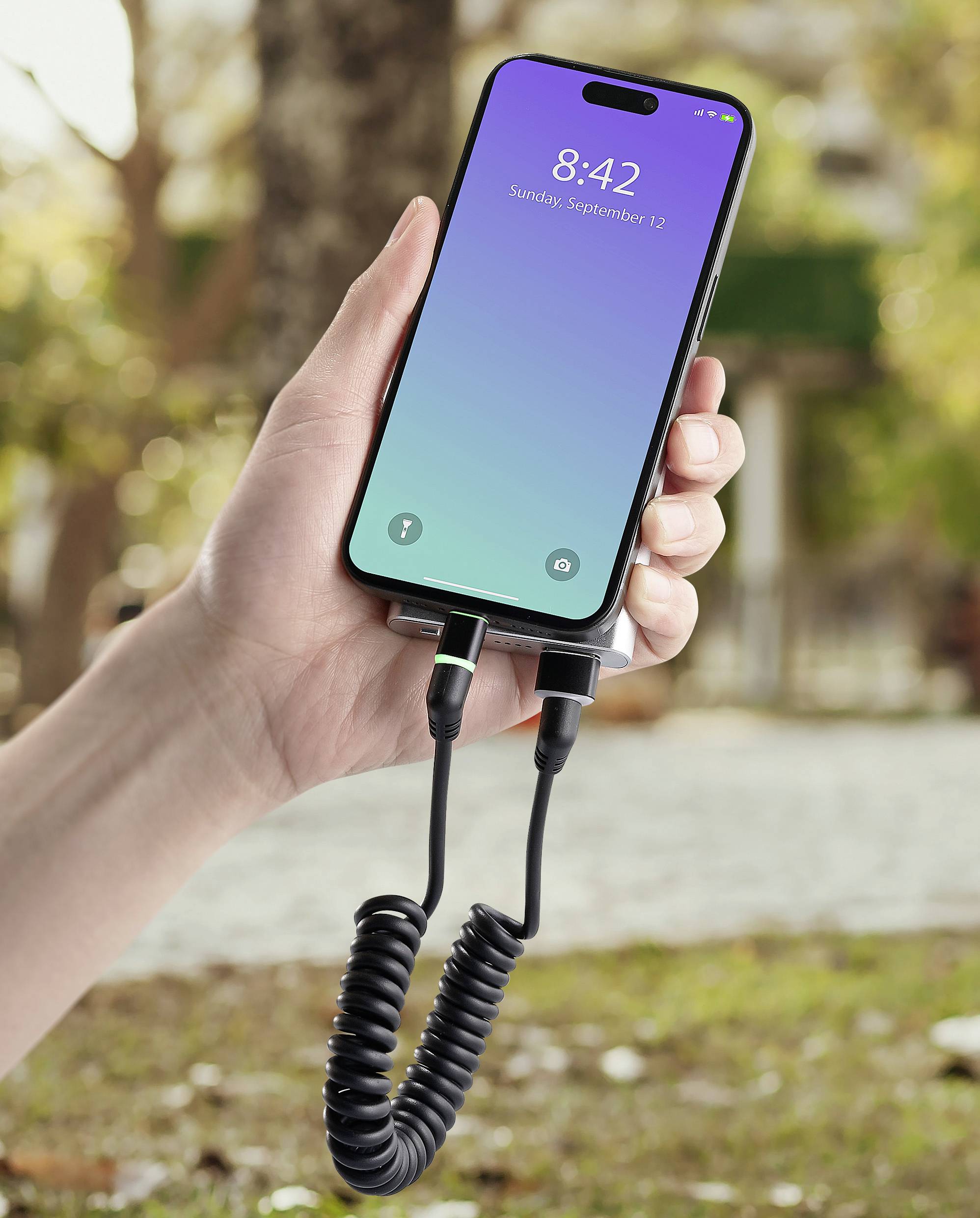 Una mano tiene uno smartphone con schermo bloccato, sul quale è visualizzato '8:42; Domenica, 12 settembre'. Il dispositivo è collegato tramite un cavo a spirale.