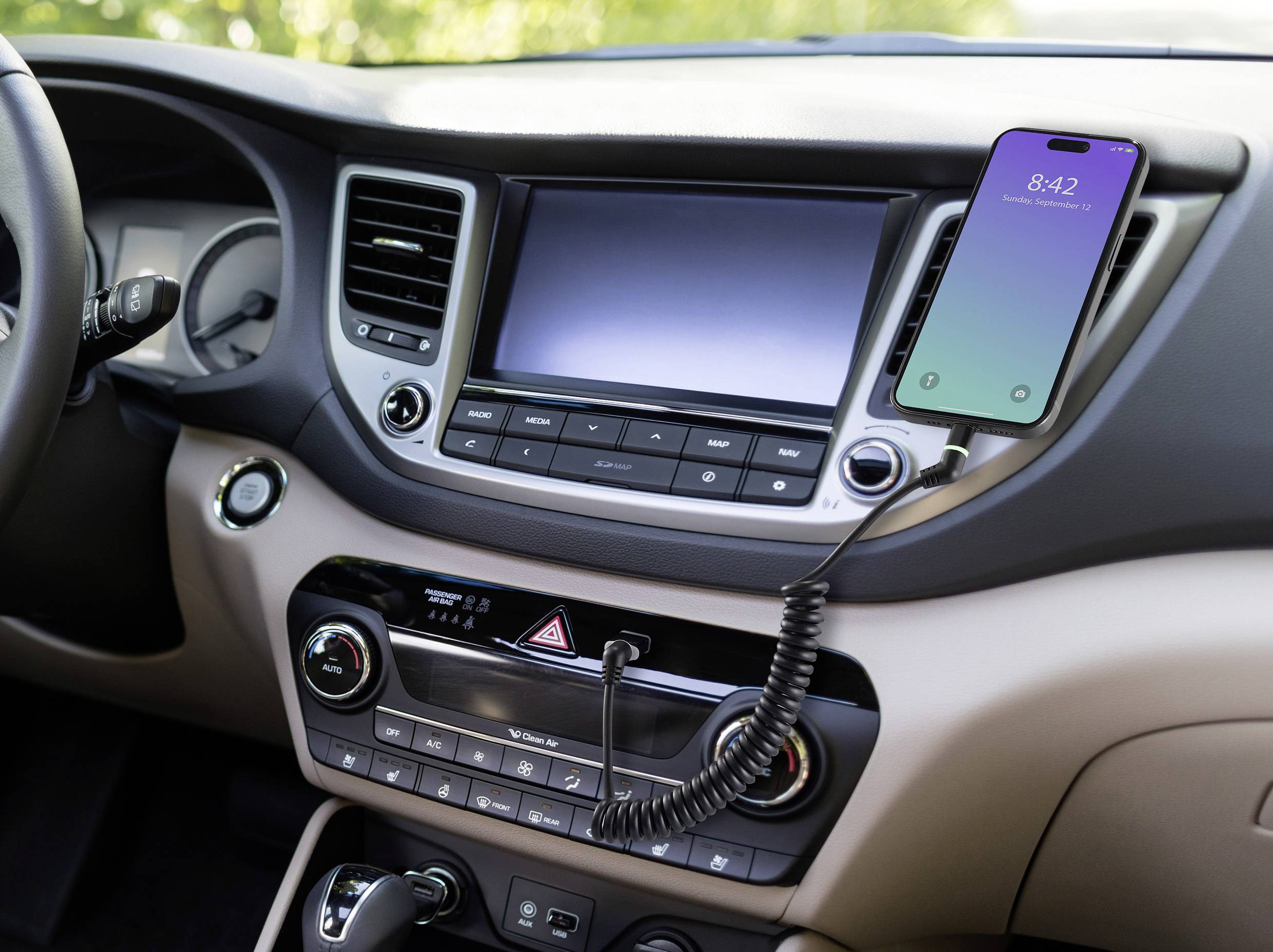 Un telefono cellulare è collegato con un cavo al cruscotto all'interno di un'auto. Il display mostra '8:42'.