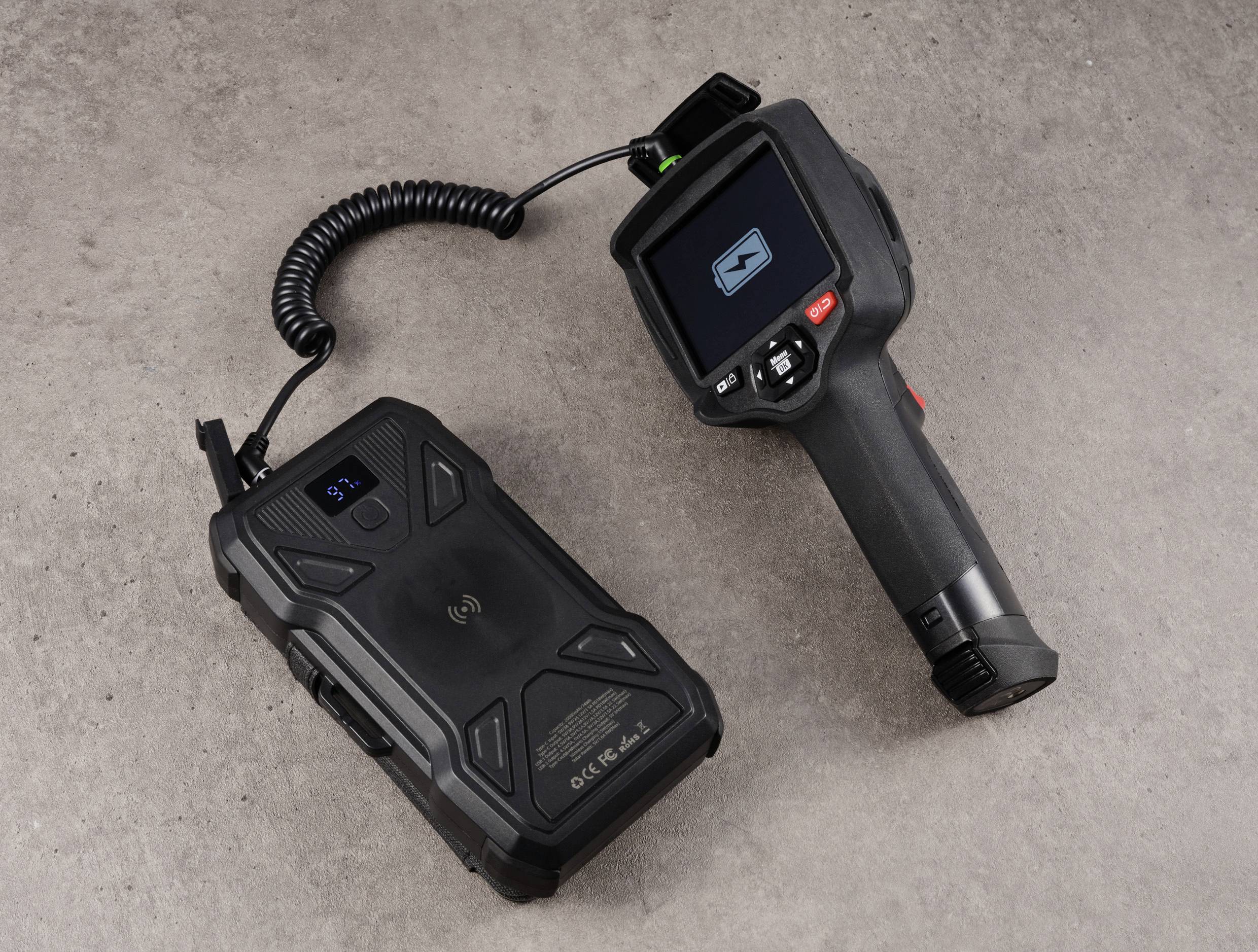 Scanner portatile di ispezione con display e impugnatura, collegati da un cavo, su una superficie grigia con texture.
