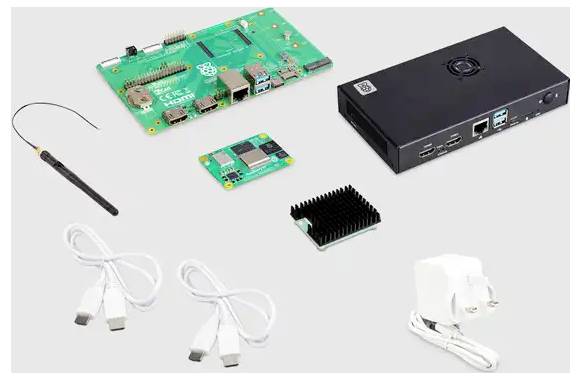 Vari componenti elettronici su un tavolo: scheda elettronica, custodia nera, antenna, adattatore e cavi.