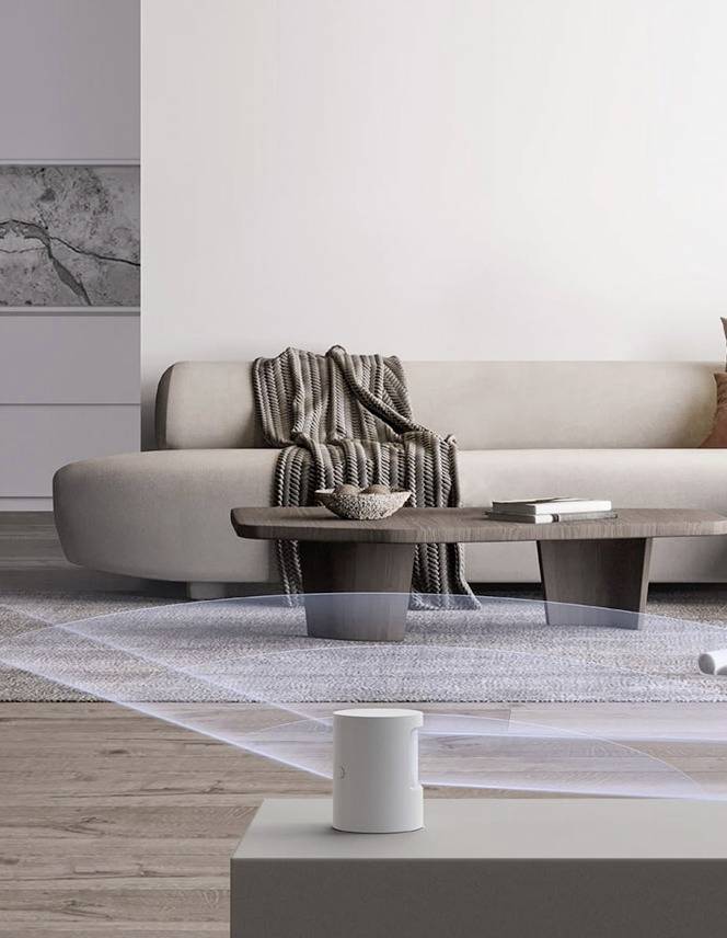 Un soggiorno moderno con un divano color crema, un tavolo in legno e una coperta a righe. In primo piano c'è un altoparlante bianco.