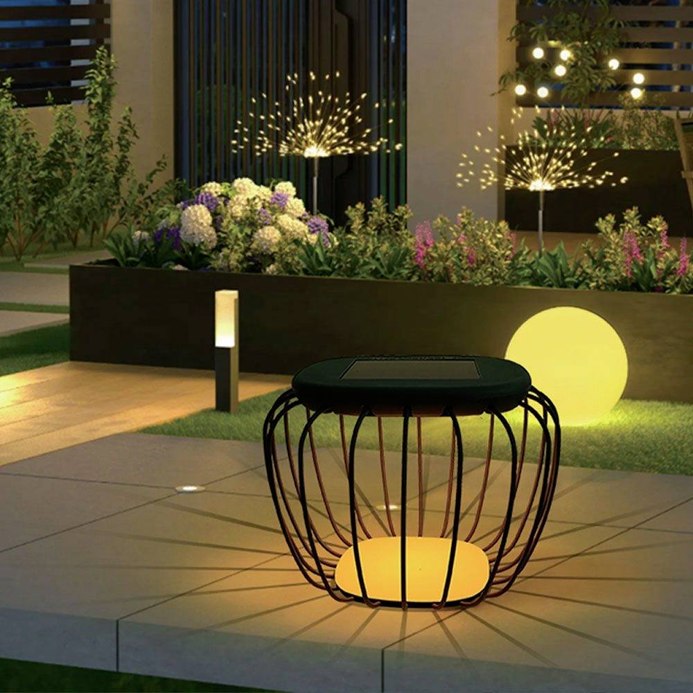 Un giardino moderno di notte con luci decorative. In primo piano un tavolo illuminato, sullo sfondo piante e una sfera luminosa rotonda.