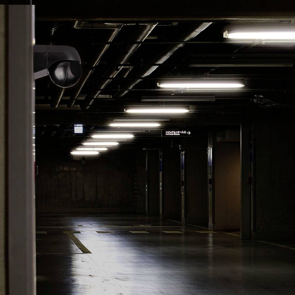 Un garage sotterraneo vuoto, poco illuminato, con una telecamera di sorveglianza visibile nell'angolo superiore sinistro.