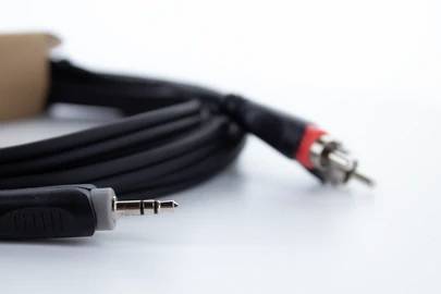 Cavo audio nero con jack da 3,5 mm e connettori RCA sullo sfondo, adagiato su uno sfondo bianco.
