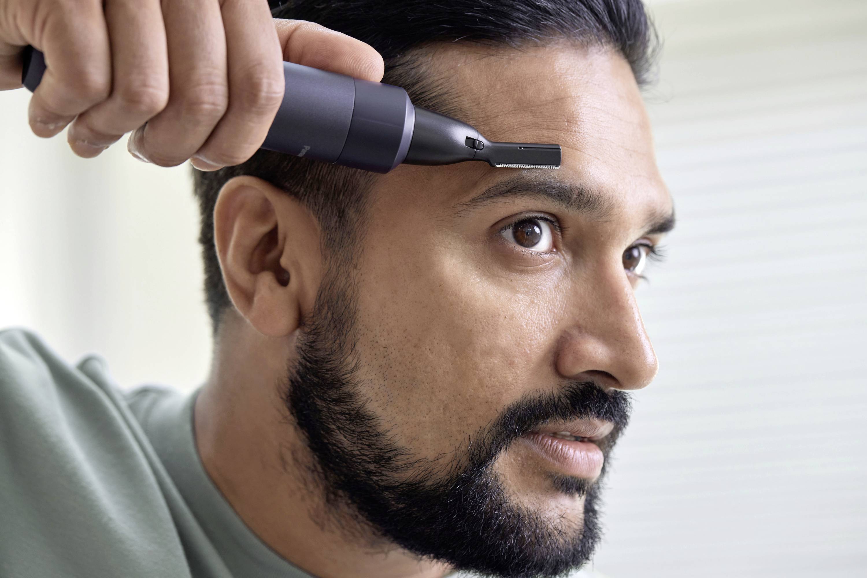 Un uomo usa un rasoio elettrico per curare la propria barba. Si concentra attentamente sul lato del suo viso.