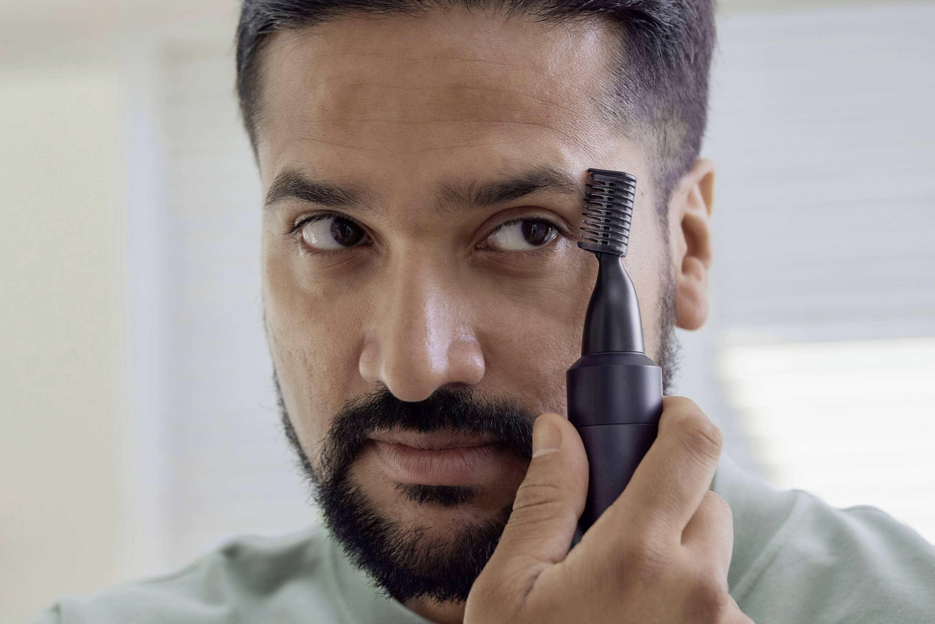 Un uomo utilizza un dispositivo elettrico per radere e sistemare le proprie sopracciglia. Si concentra sullo styling preciso.