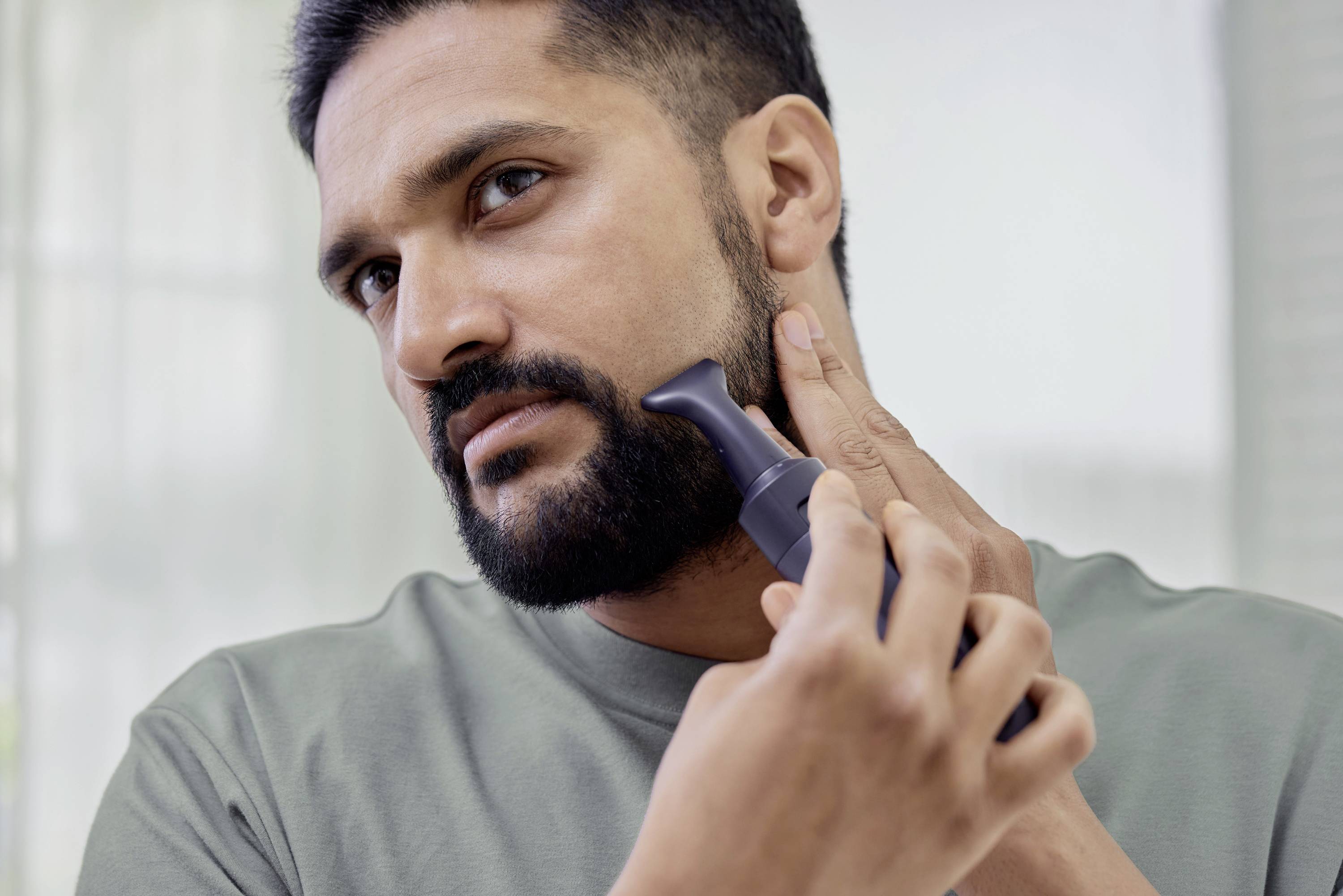 Un uomo usa un rasoio elettrico per curare la propria barba in una stanza ben illuminata.