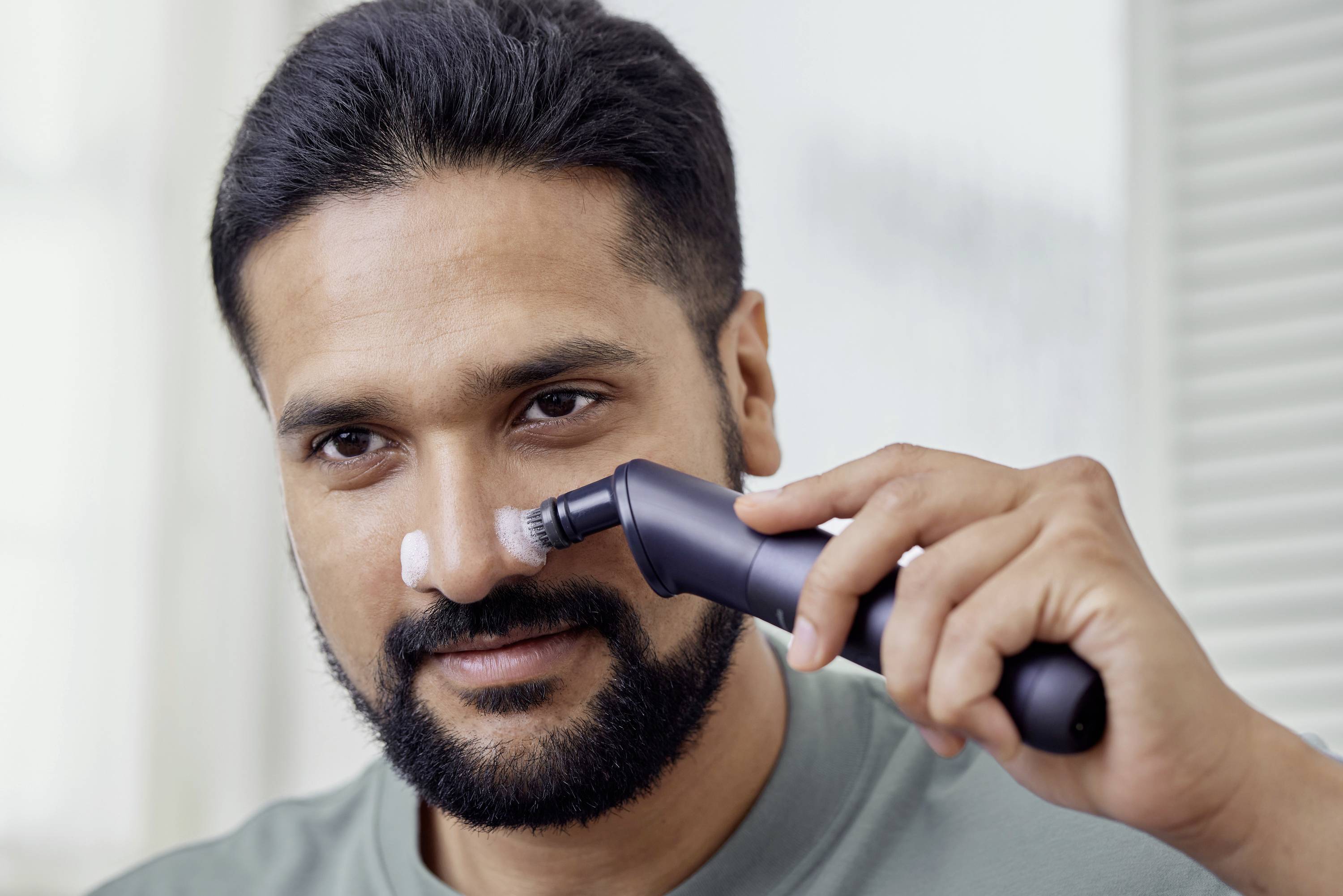 Un uomo applica una crema o lozione sul proprio viso con un dispositivo elettronico.