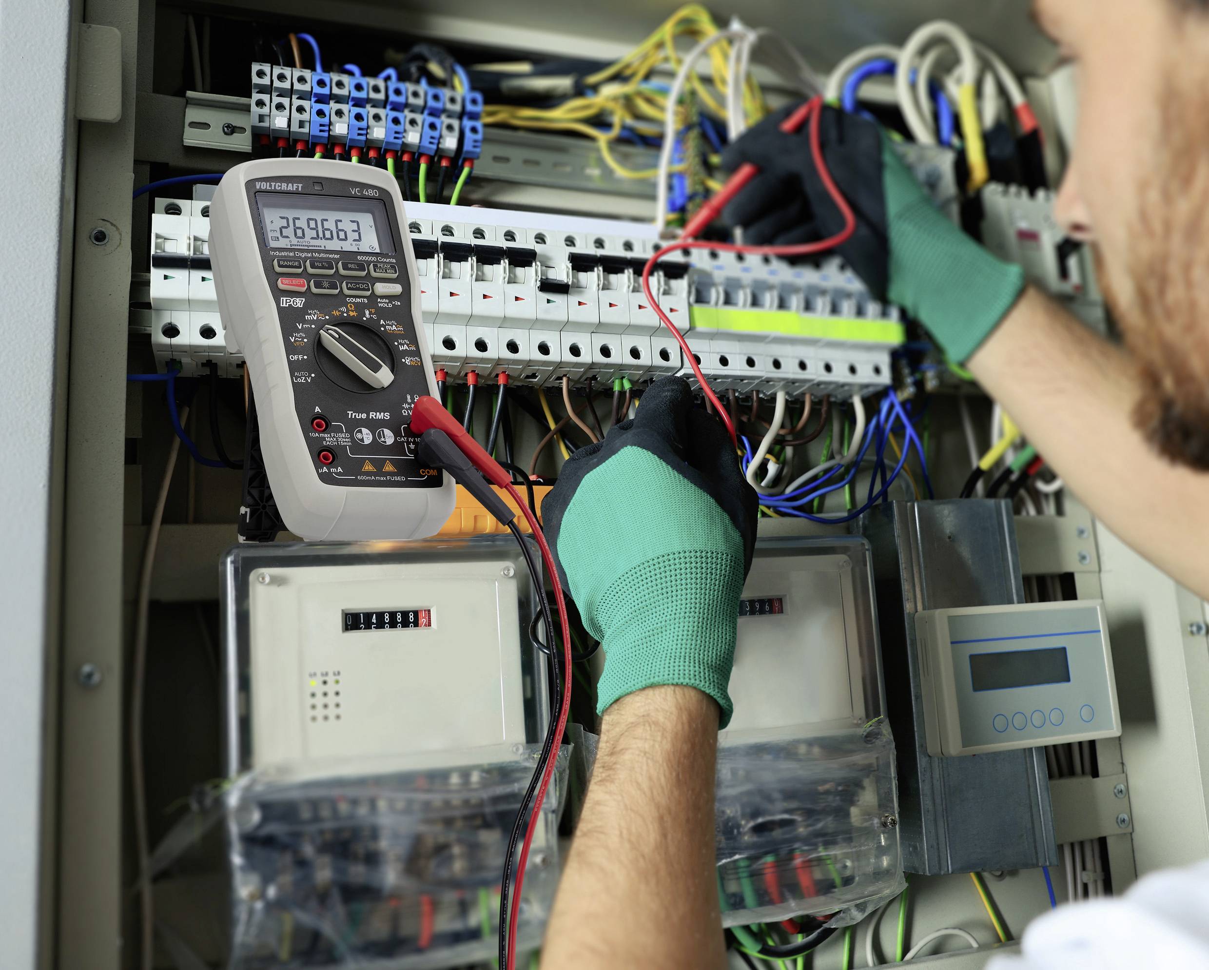 Un tecnico sta verificando le connessioni elettriche in un quadro elettrico utilizzando un multimetro che mostra un valore di 269,663.