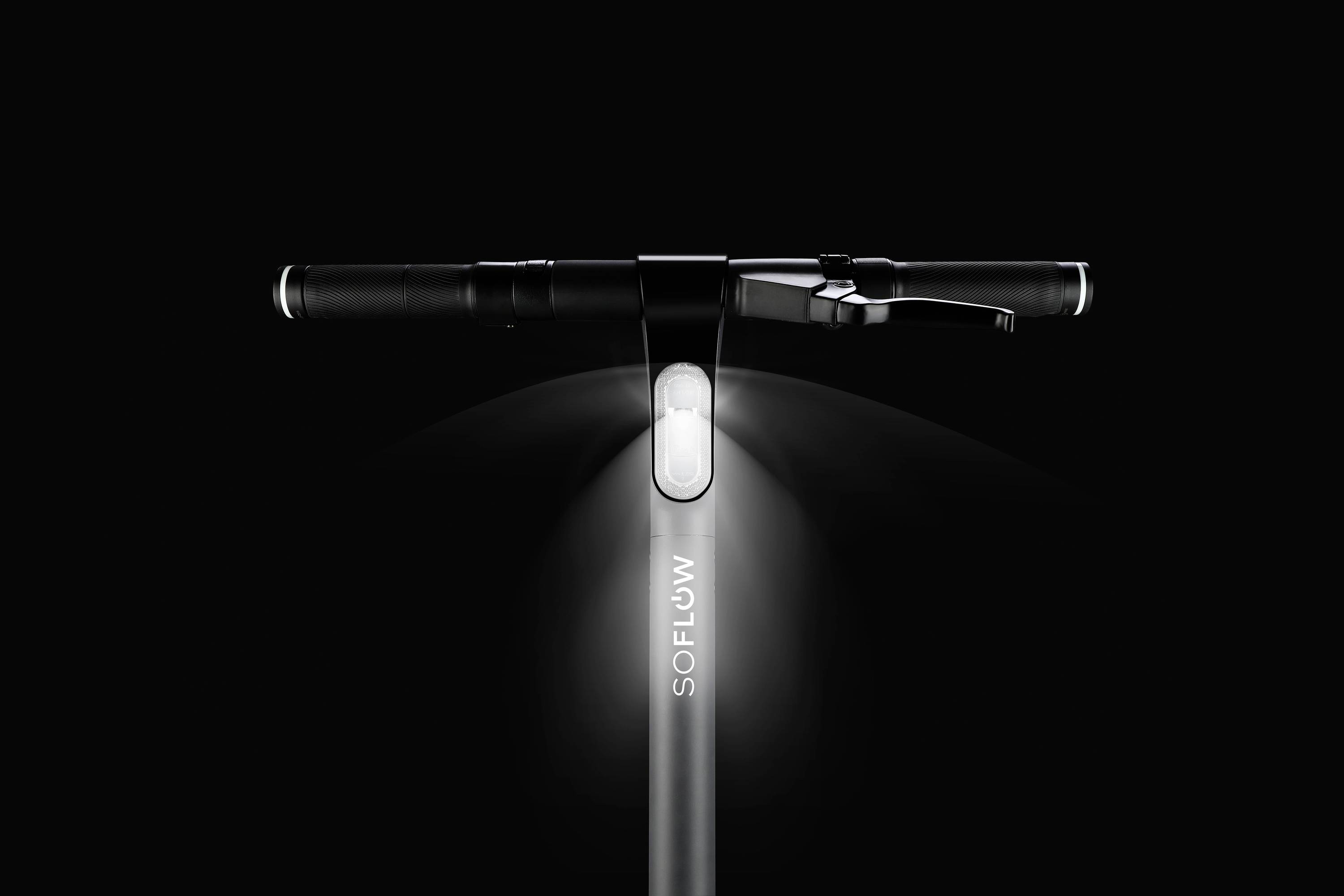 Un manubrio di monopattino elettrico nero con un faro anteriore illuminato e la scritta 'SOFLOW'. Lo sfondo è scuro.
