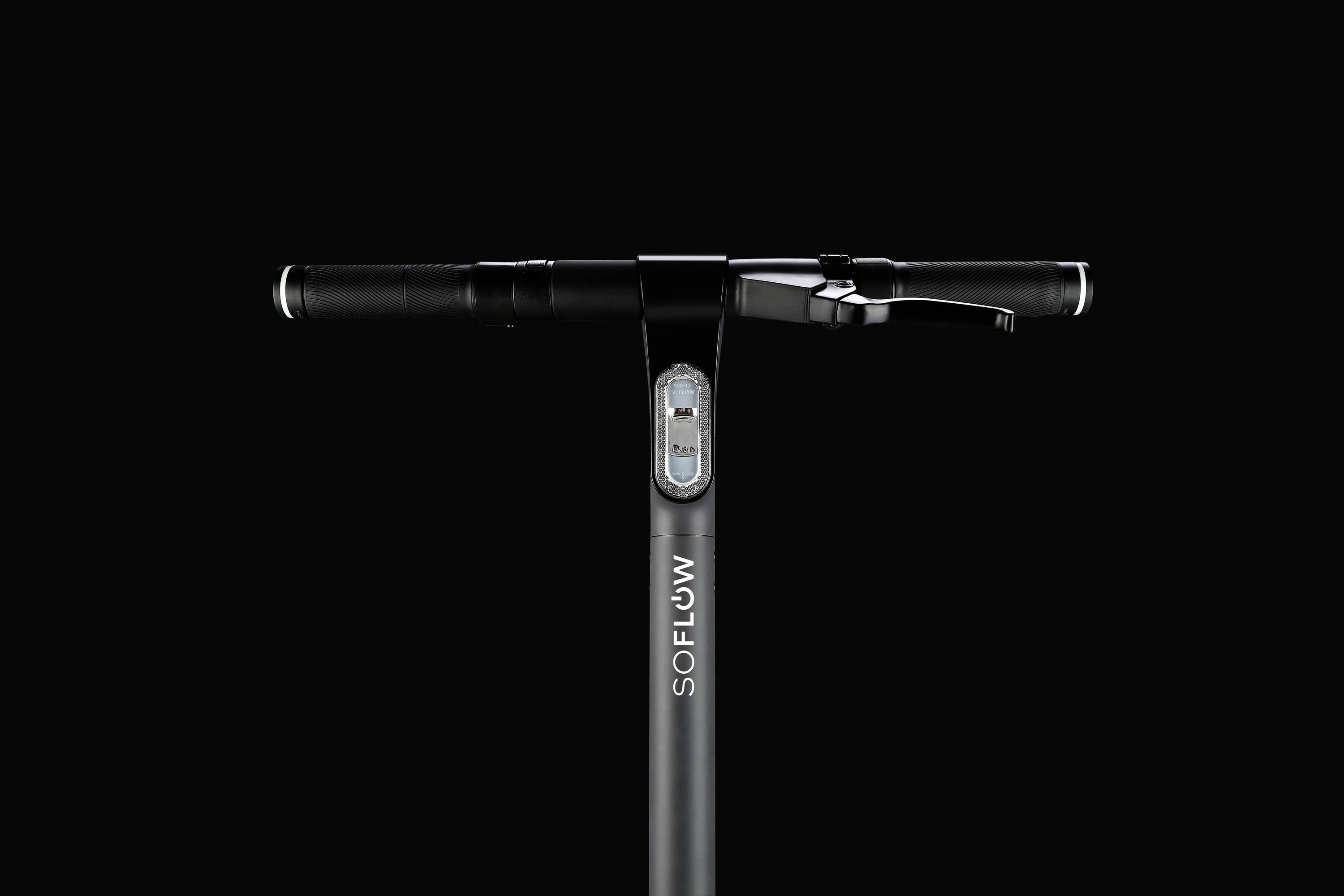 Manubrio di un monopattino elettrico con display centrale, logo aziendale 'SOFLOW' sul tubo. Design in nero su sfondo nero.