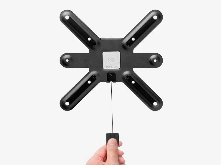 Una mano tiene un supporto da parete per TV a forma di X nero, con un cavo sulla parte inferiore.