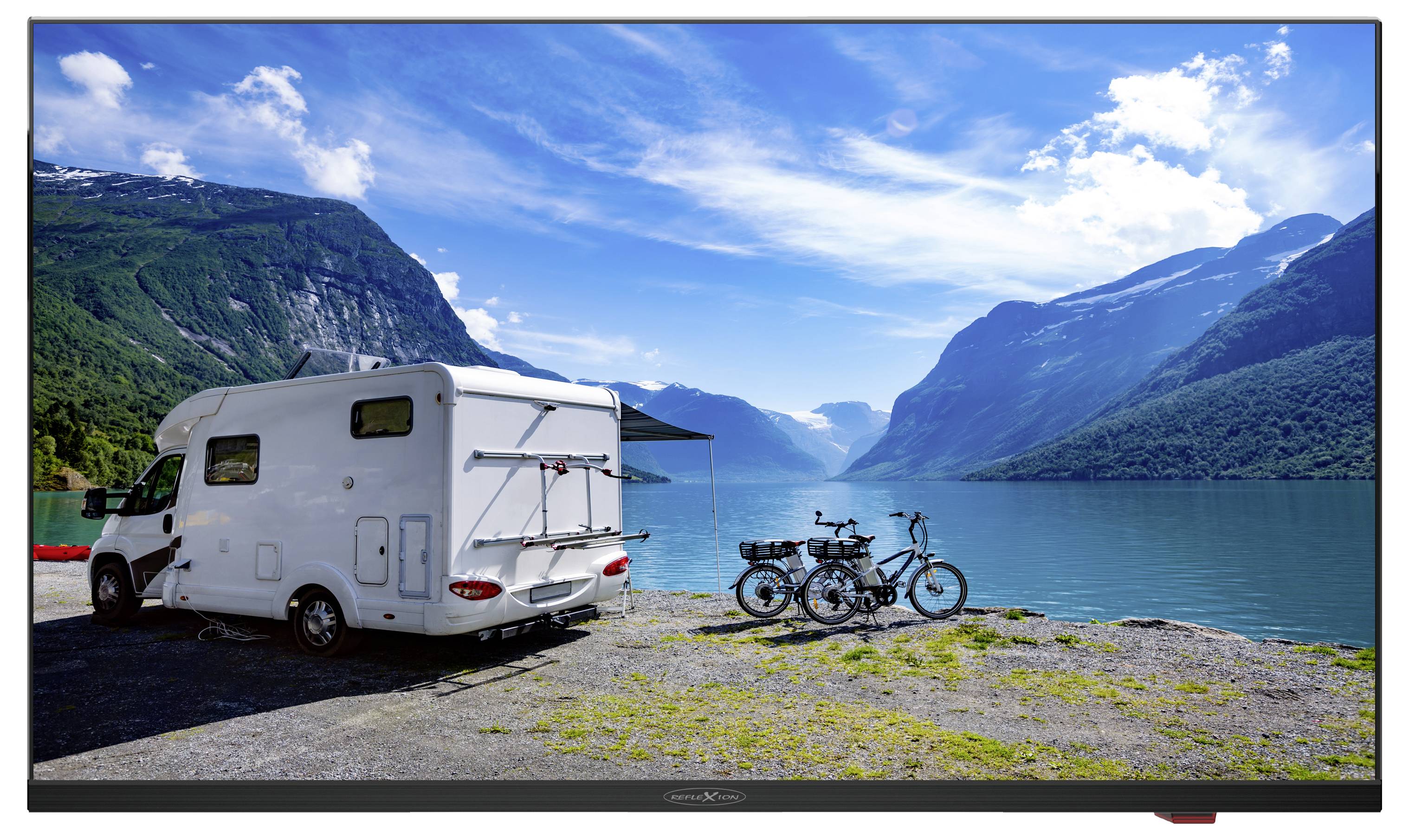 Un camper è parcheggiato sulla riva di un lago pittoresco, circondato da montagne. Due biciclette sono parcheggiate accanto al camper. Cielo limpido.