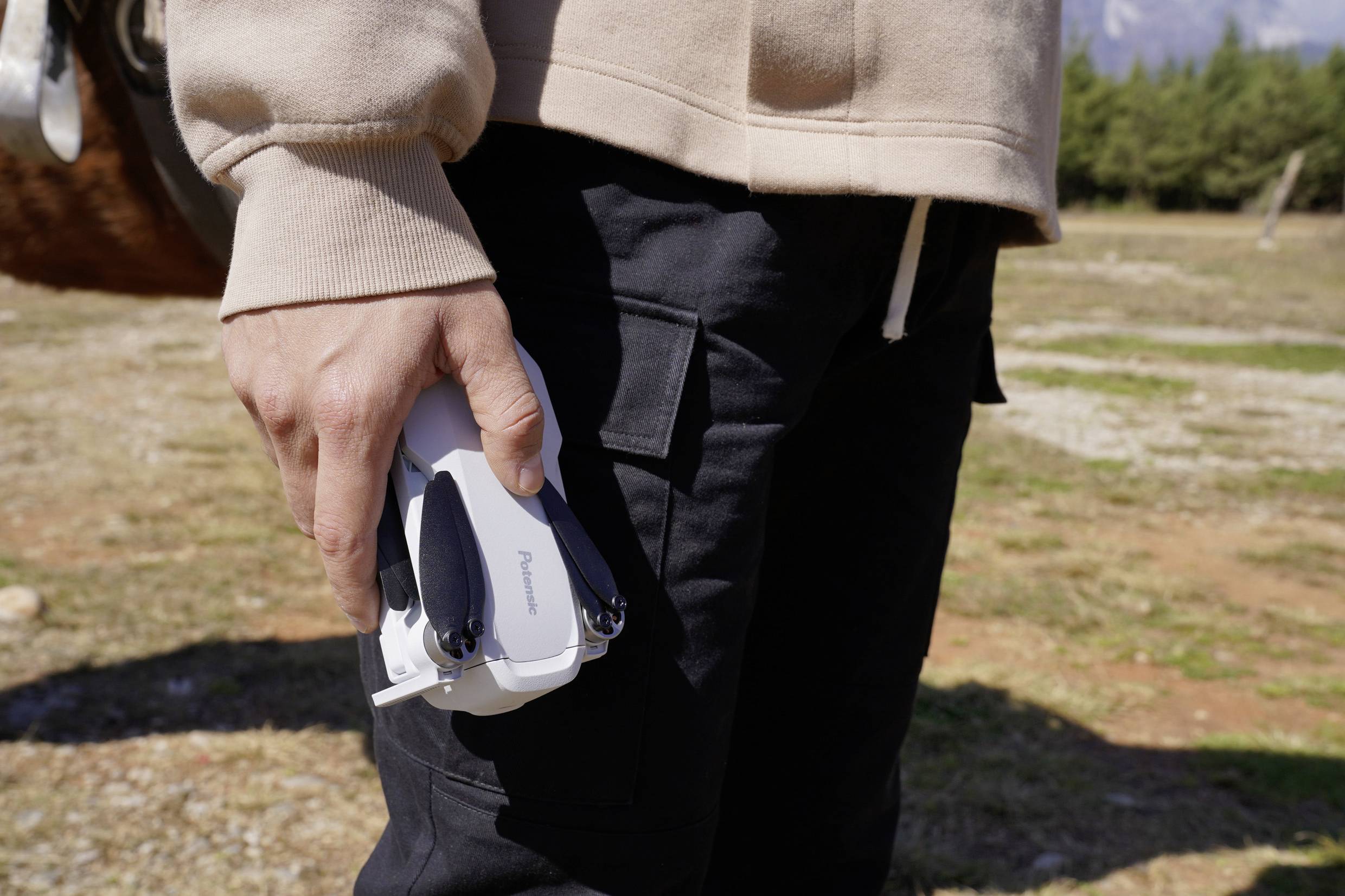 Una persona tiene un piccolo drone in mano, pronta al decollo in un ambiente naturale con tempo soleggiato.