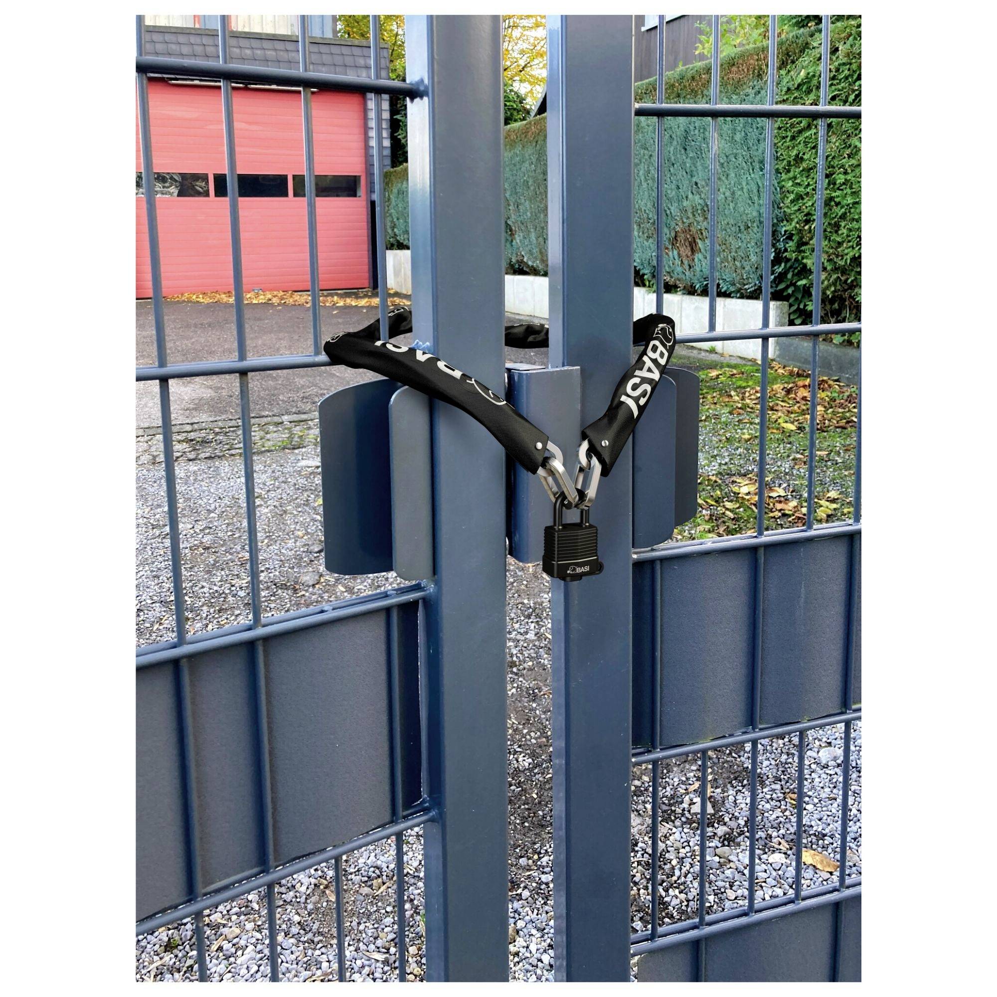 Un cancello metallico blu è assicurato con una catena nera e un lucchetto. Sullo sfondo si vedono alberi e portoni di garage rossi.
