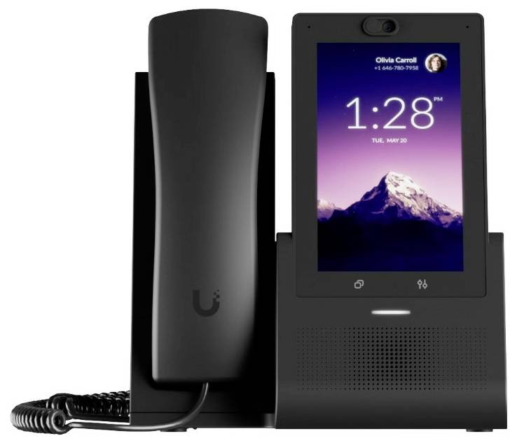 Un telefono da tavolo digitale con schermo touch mostra l'ora '1:28 PM'. Sullo sfondo è visibile un'immagine di montagna.