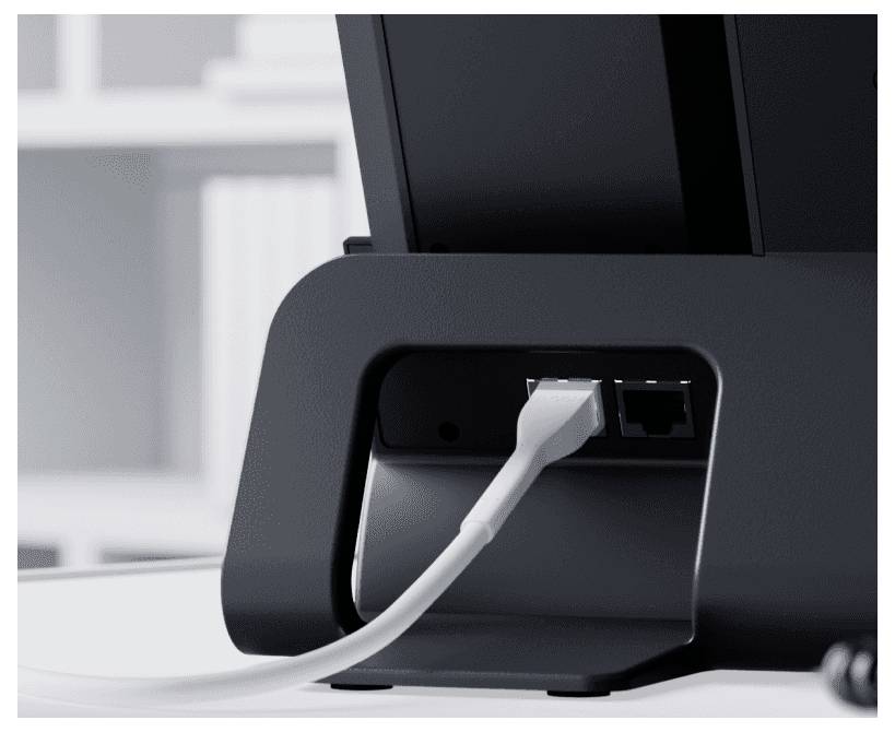 Un cavo Ethernet viene collegato alla porta posteriore di un monitor, con uno scaffale di libri sfocato sullo sfondo.