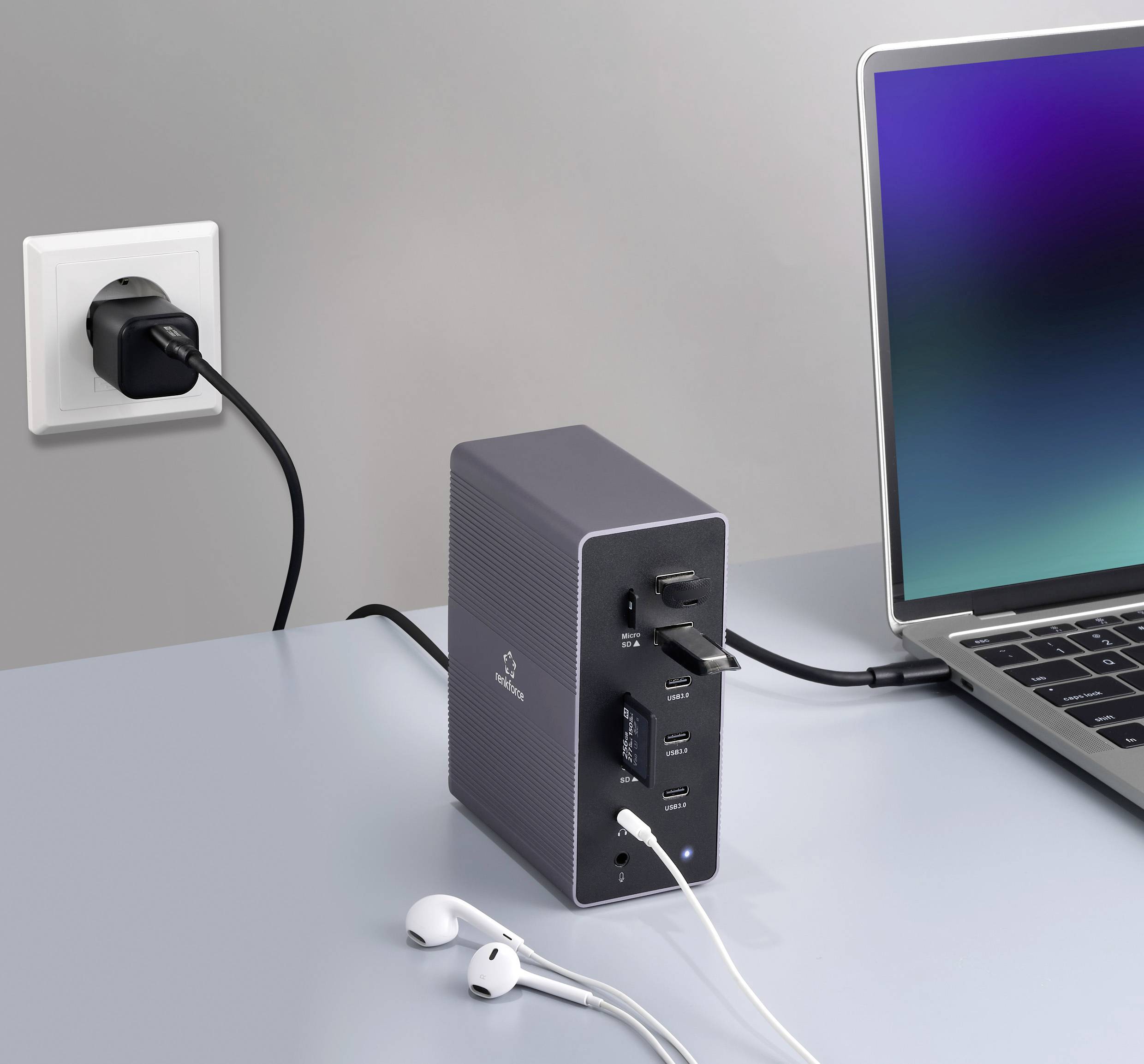 Un laptop è collegato a una stazione di aggancio connessa a una presa elettrica. Delle cuffie sono posizionate accanto.