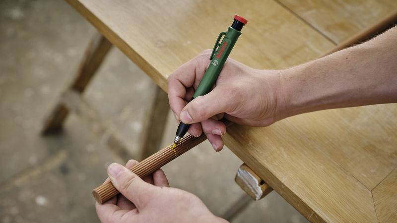 Qualcuno traccia una linea con una penna su un pezzo di legno sopra un tavolo.