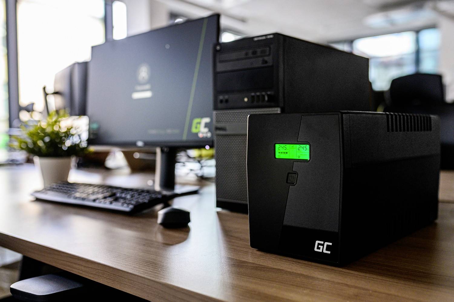 Una scrivania con un monitor del computer, una tastiera e un'unità di alimentazione di continuità (UPS) di GC in primo piano.