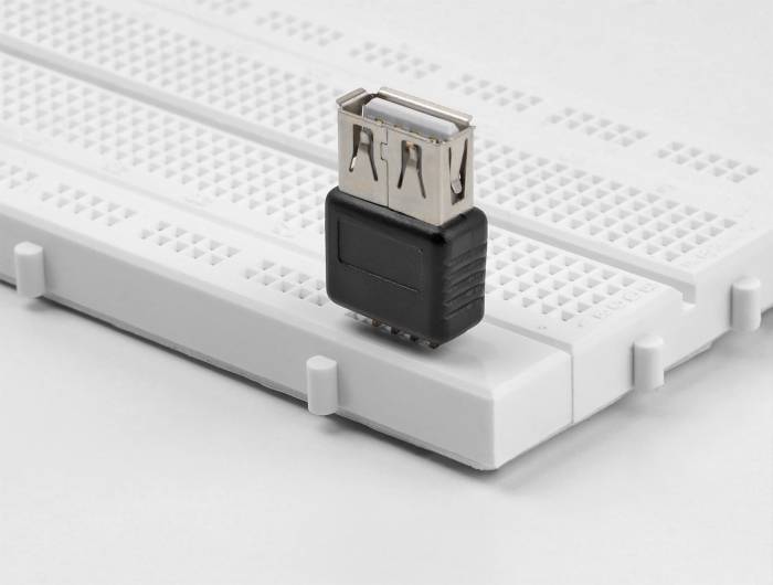 Un adattatore USB nero è posizionato su una breadboard bianca, utilizzata per la prototipazione di circuiti elettronici.