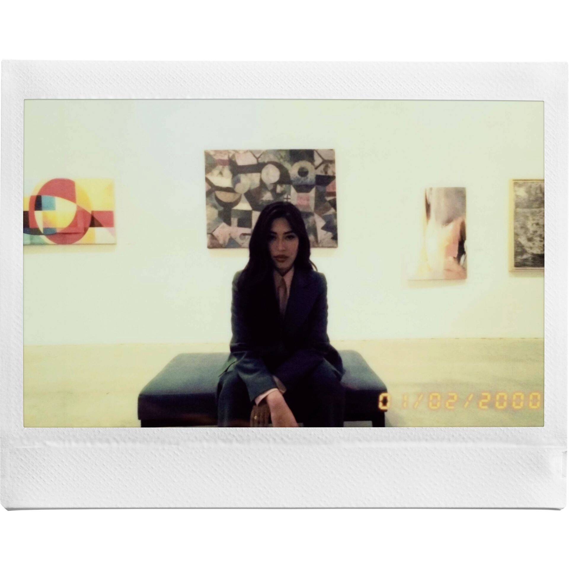 Una persona è seduta su una panchina in una galleria d'arte. Sullo sfondo, dipinti astratti sono appesi alla parete.