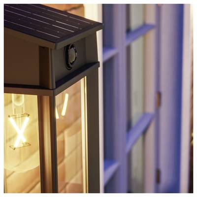 Primo piano di una lanterna da esterno nera con una lampadina che brilla montata accanto a una finestra.